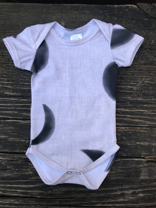 Short sleeve moon phase onesie on a wood bench