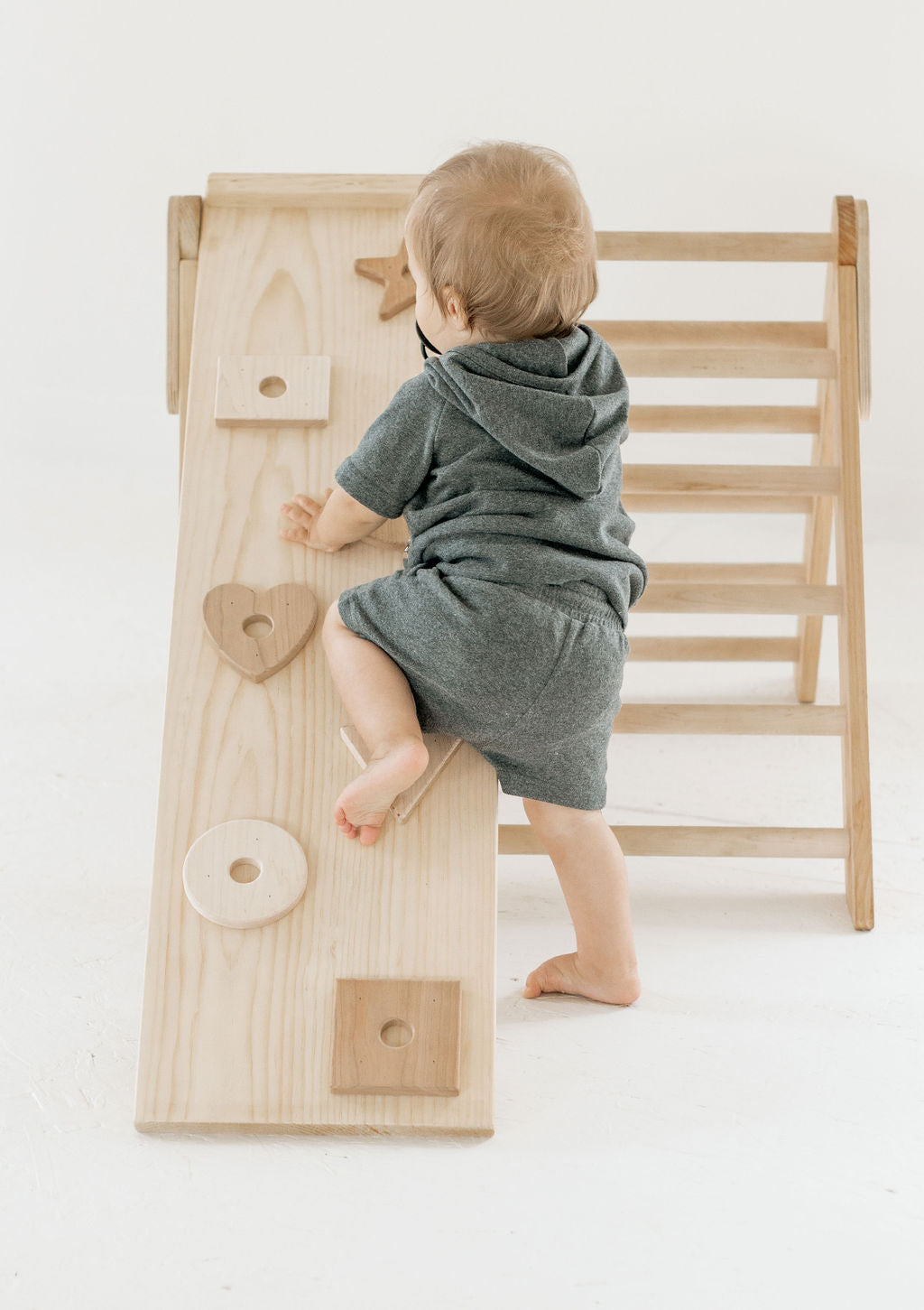 Child playing with a wooden climbing toy on a white floor