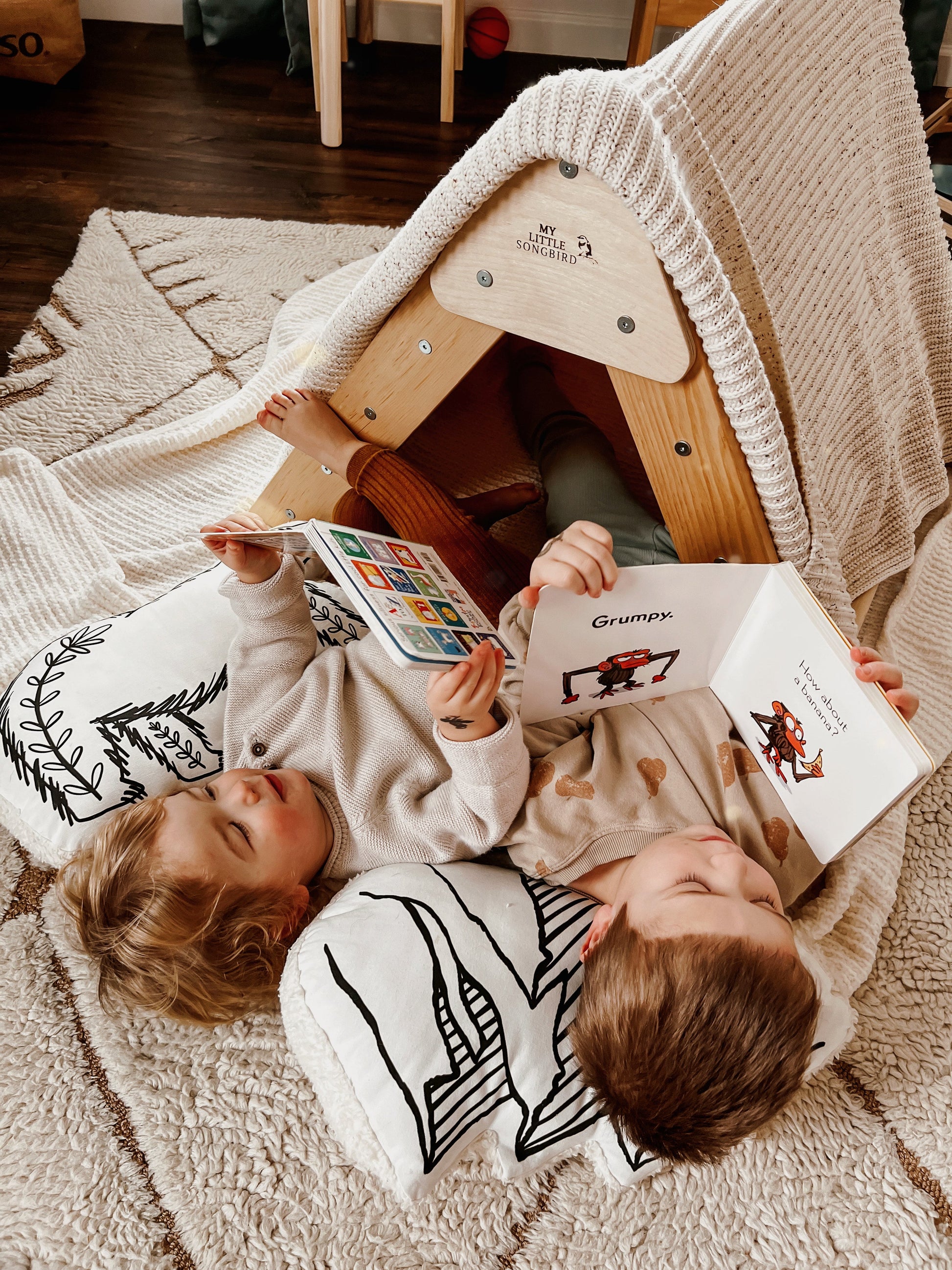 Two children lying on a rug inside a wooden playhouse, reading books.