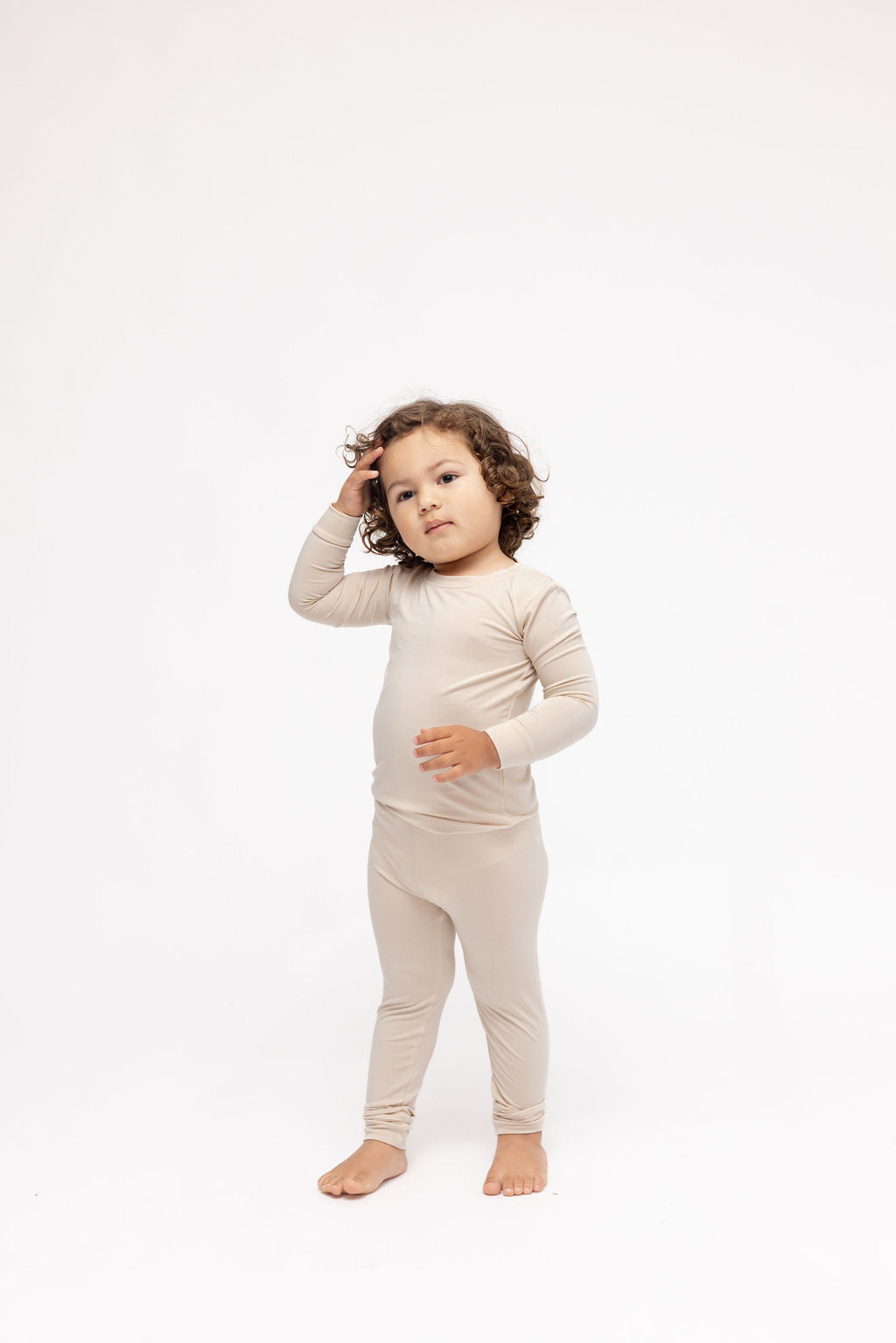 Child wearing a beige long-sleeve shirt and pants on a white background