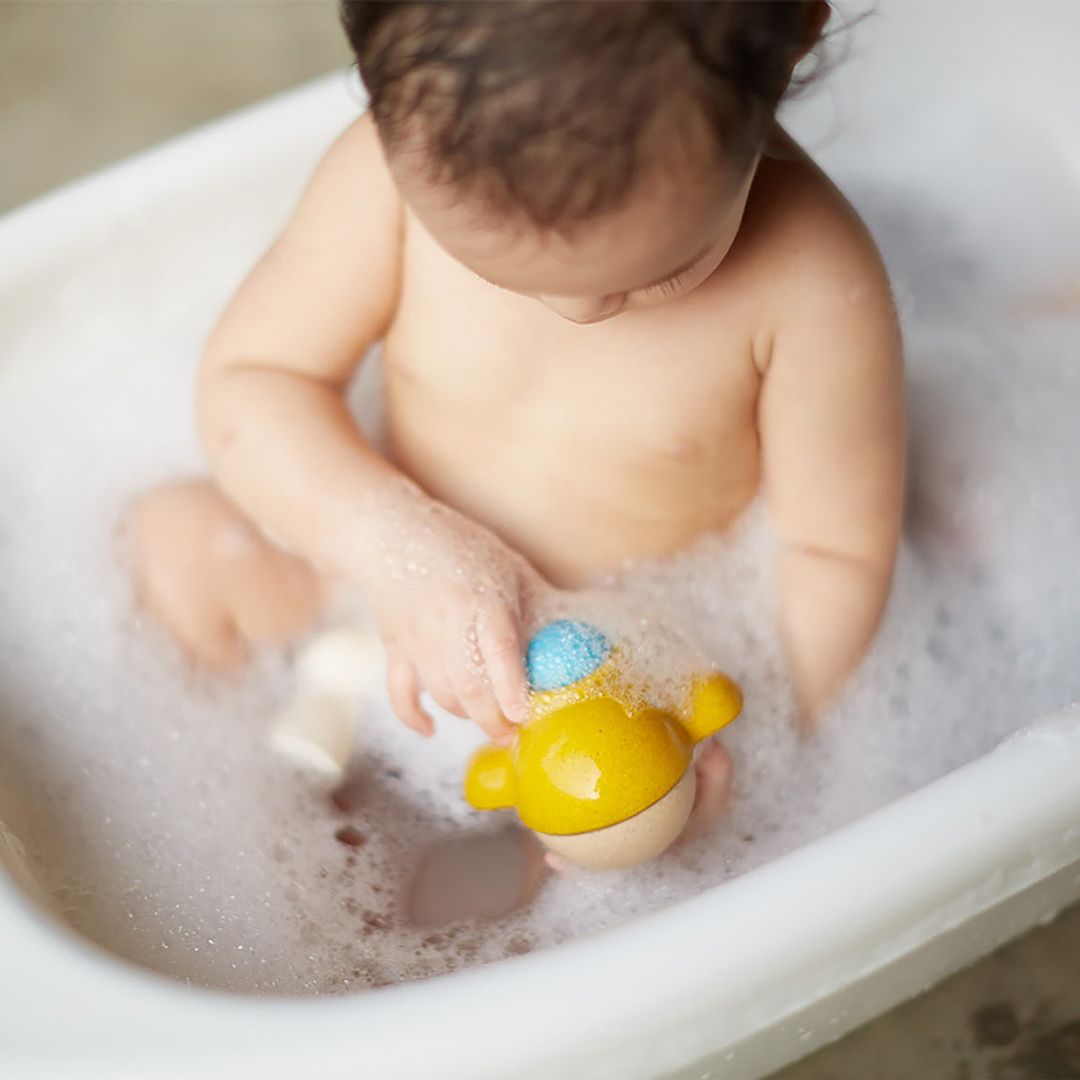 Baby playing with a yellow toy in a bathtub filled with bubbles