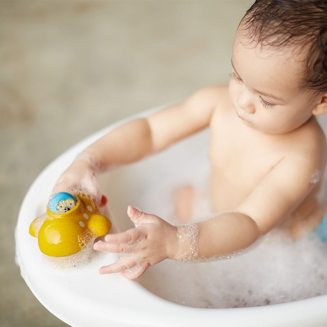 Baby playing with a yellow rubber duck in a bathtub filled with bubbles.