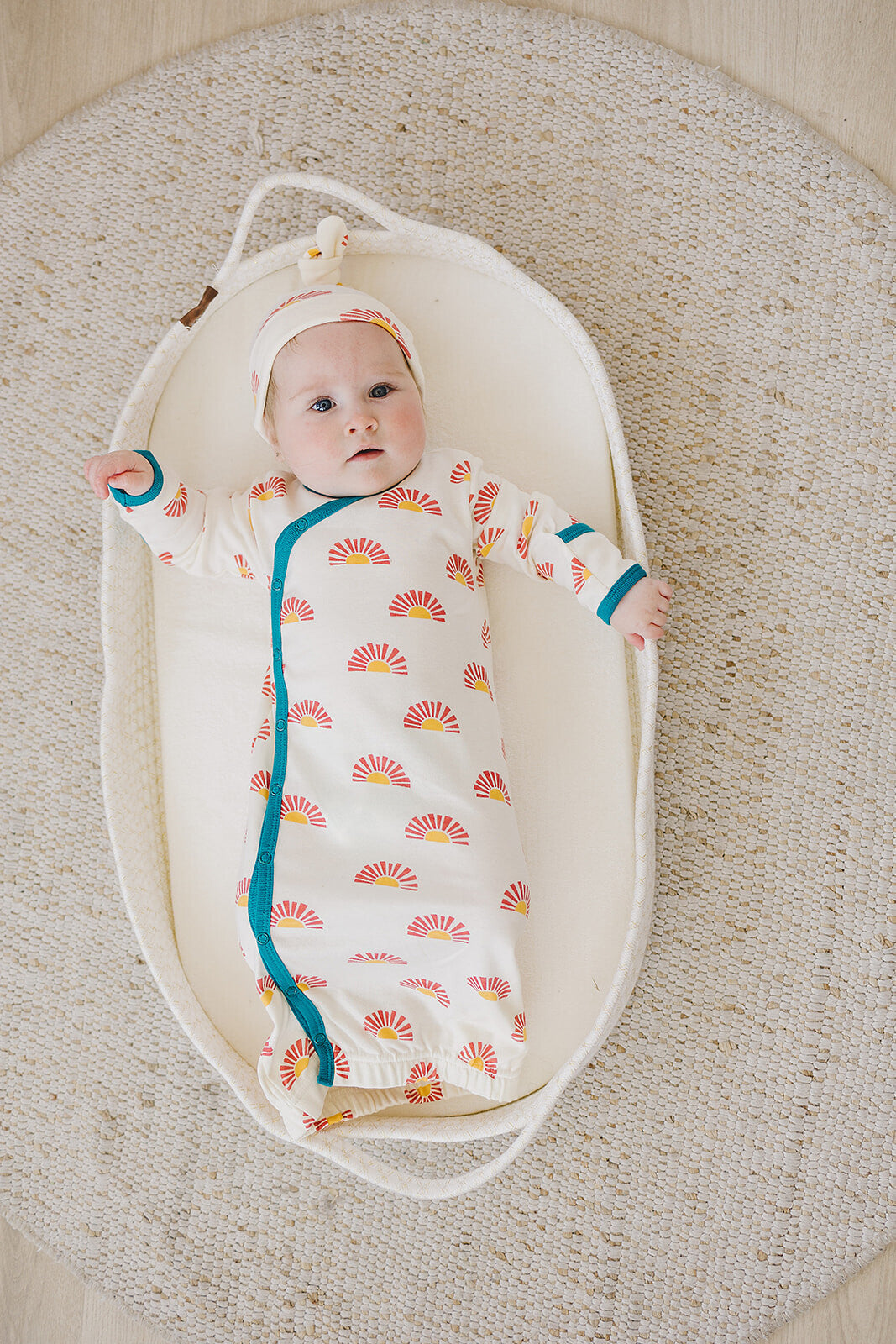 Baby in a swaddle with sun pattern lying in a bassinet on a textured surface