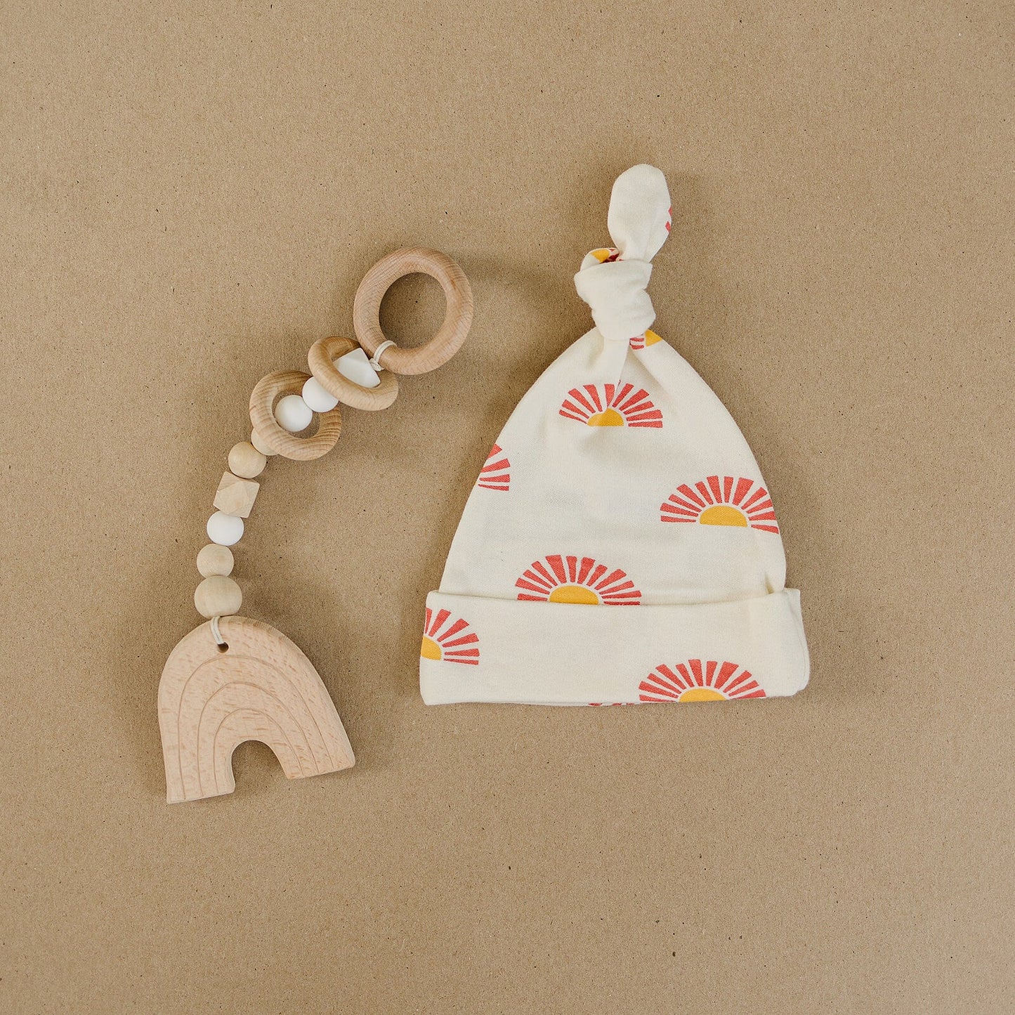 Wooden teething toy and baby hat with sun pattern on a brown background