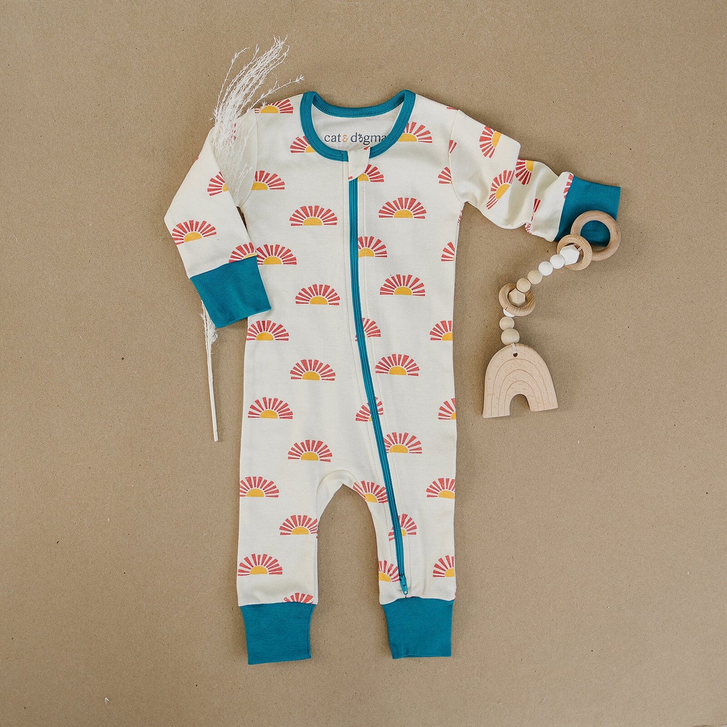 Baby onesie with sun pattern and blue accents, accompanied by a wooden teething toy on a brown background.