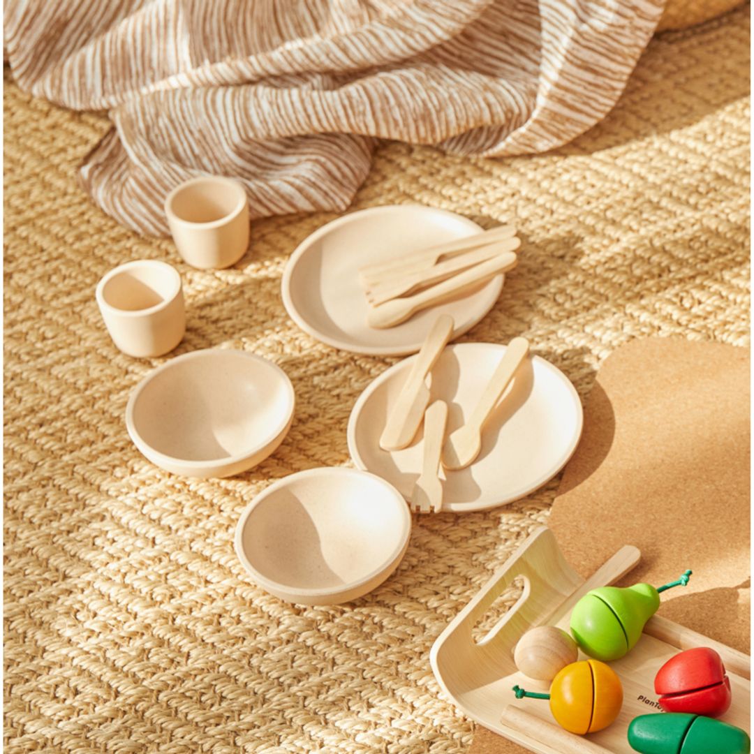 Set of wooden toys including bowls, spoons, and a colorful caterpillar toy on a textured surface.