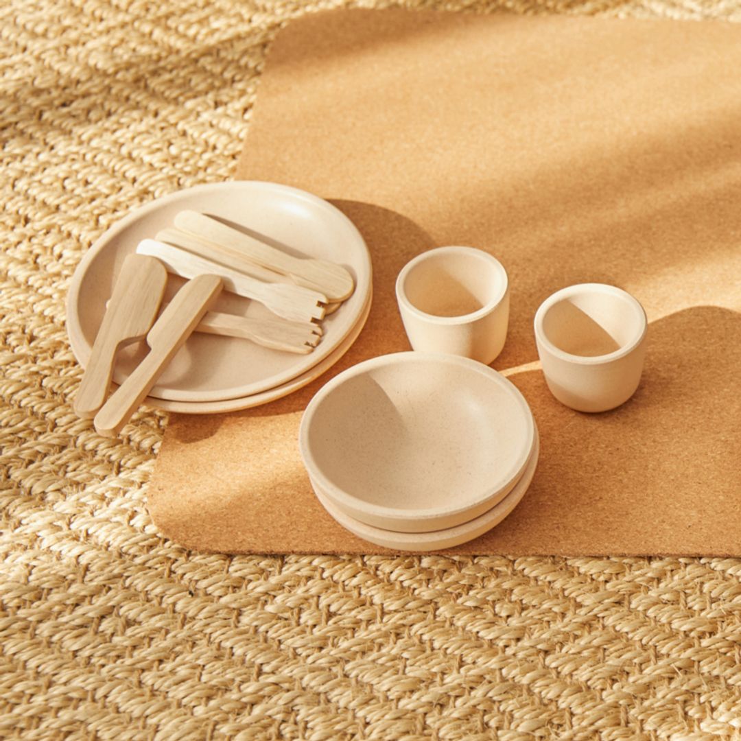 Set of beige ceramic dishes including plates, bowls, and cups on a textured surface.