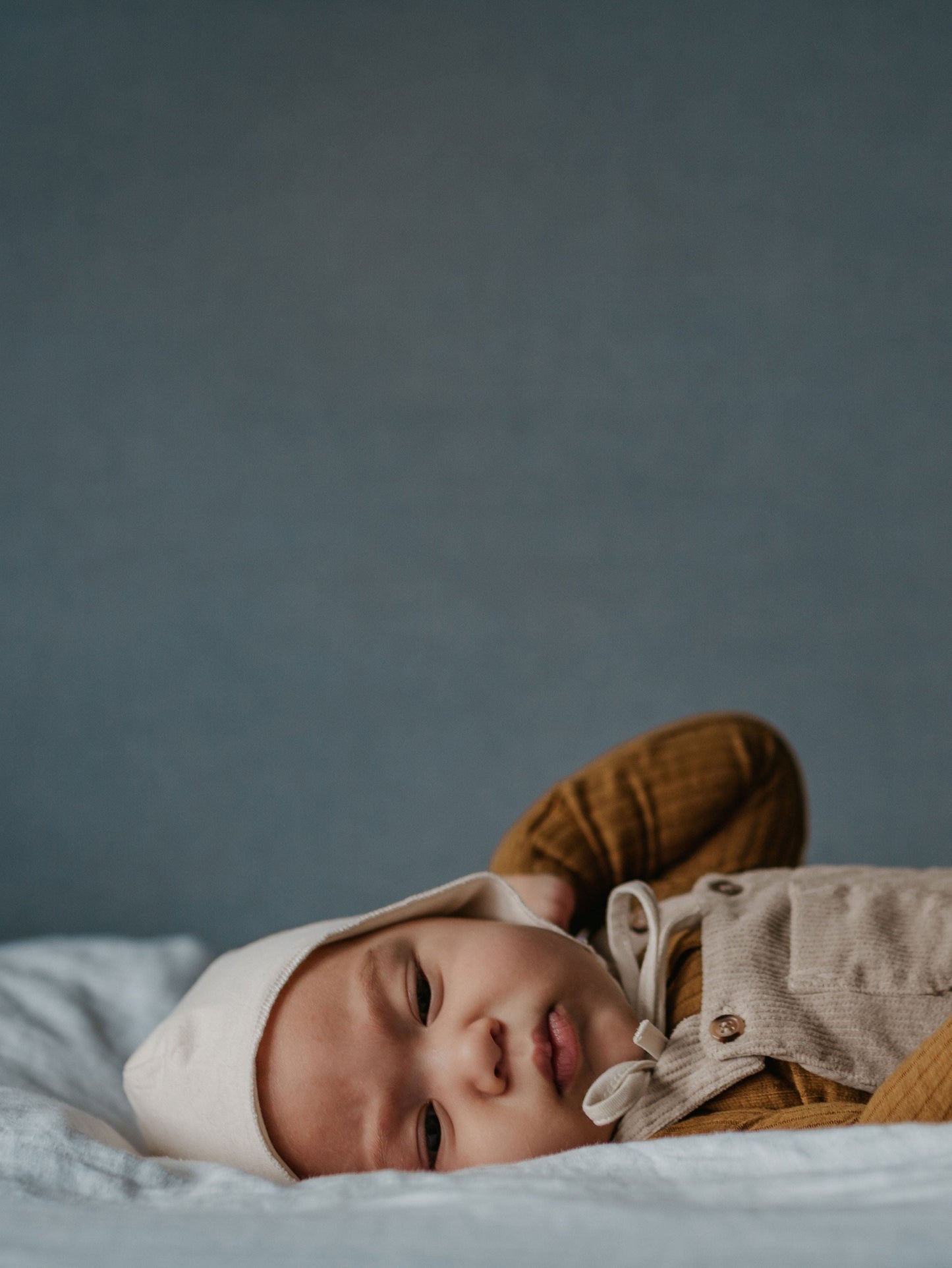 Newborn baby wearing a beige outfit and hat on a blue background