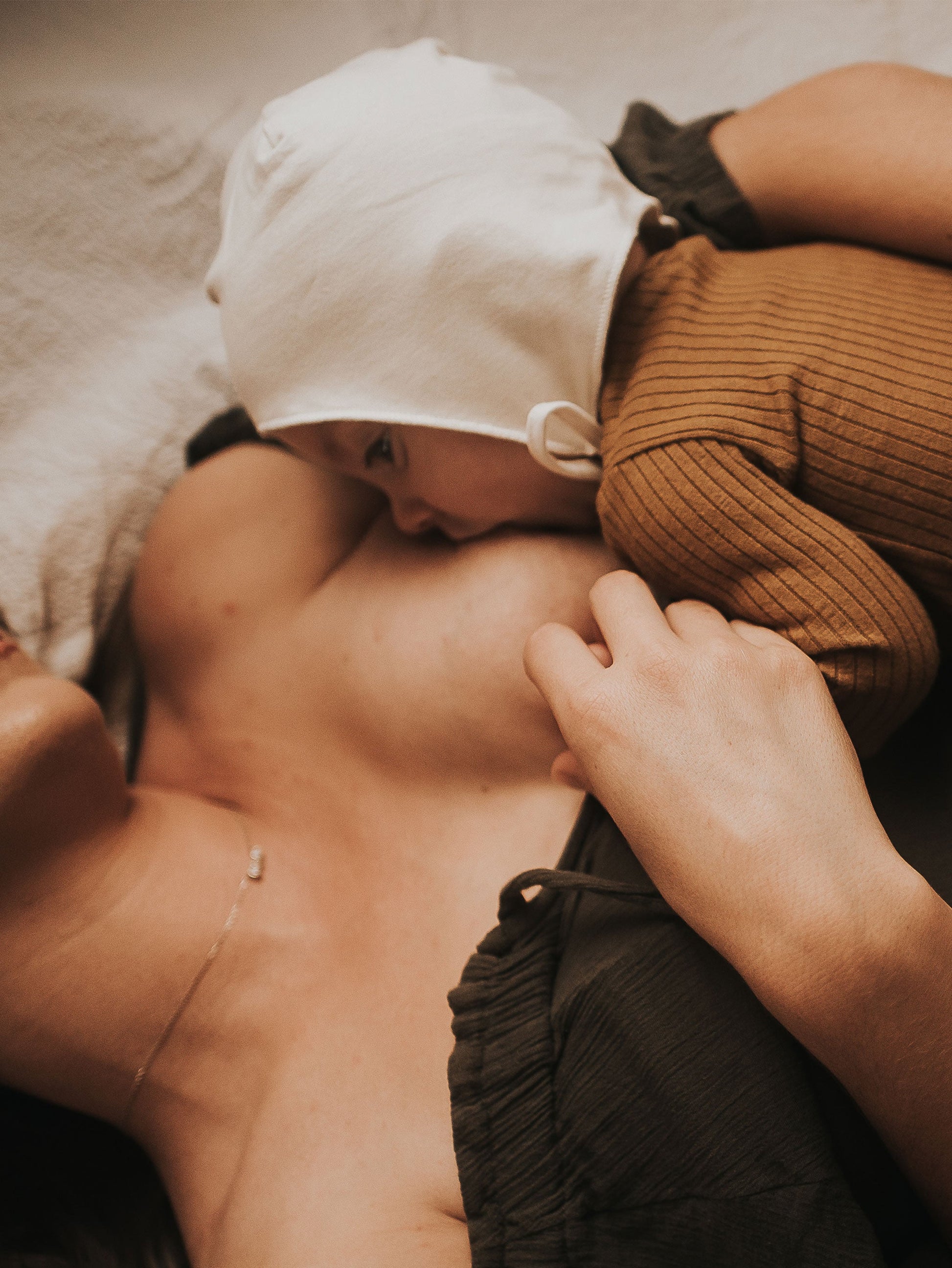 Person holding a baby wrapped in a brown blanket on a bed.