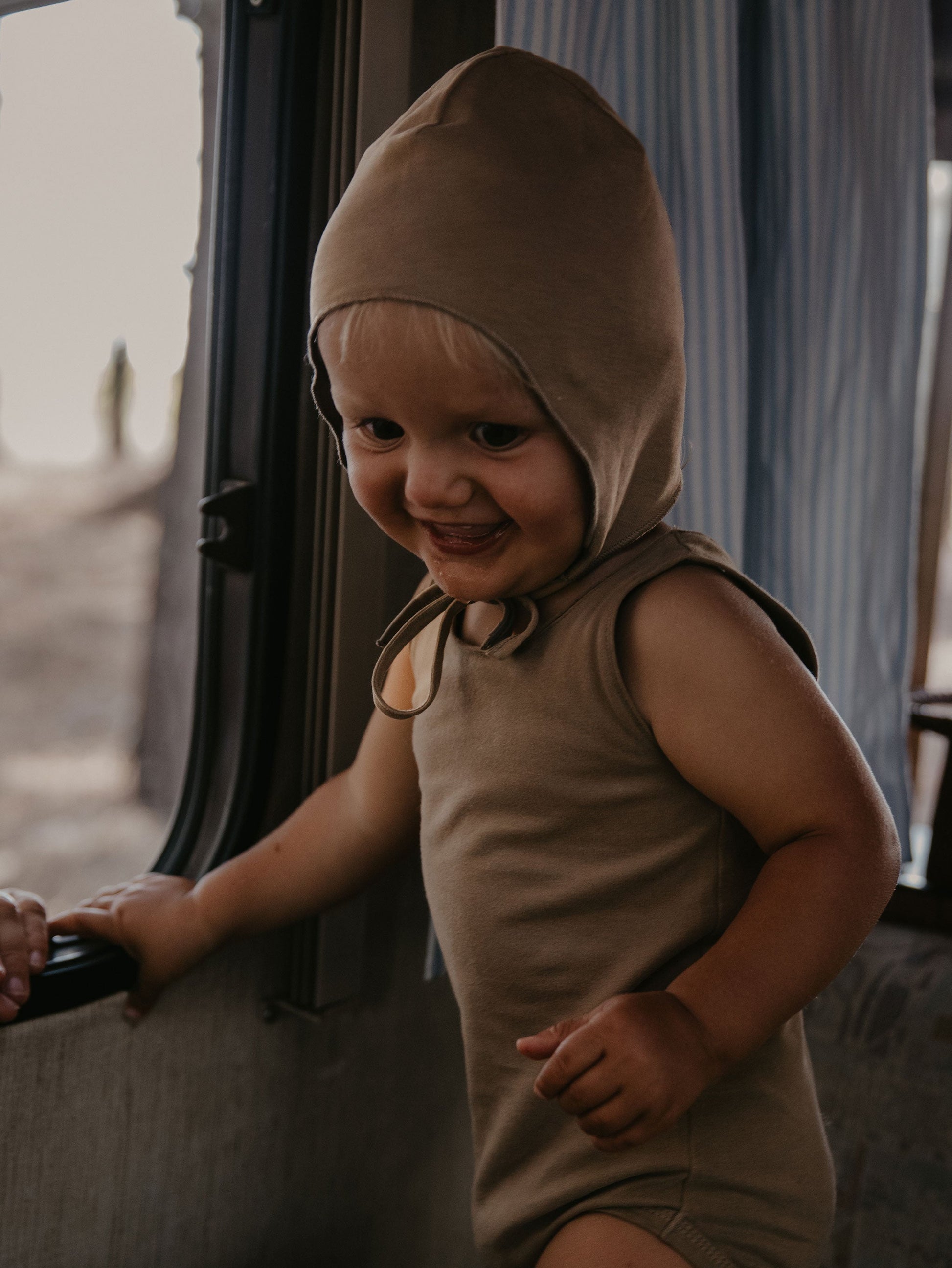 Child wearing a brown hooded outfit standing inside a vehicle.