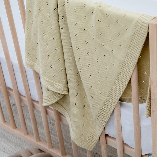 Beige textured blanket draped over a crib with white bedding.