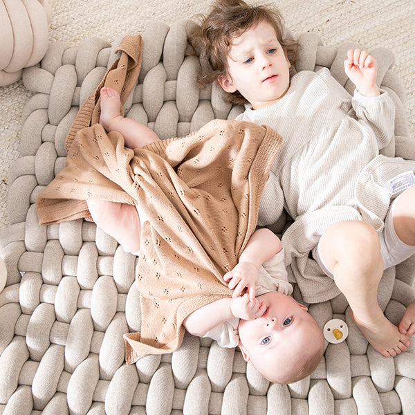 Two children lying on a textured rug, one holding a baby
