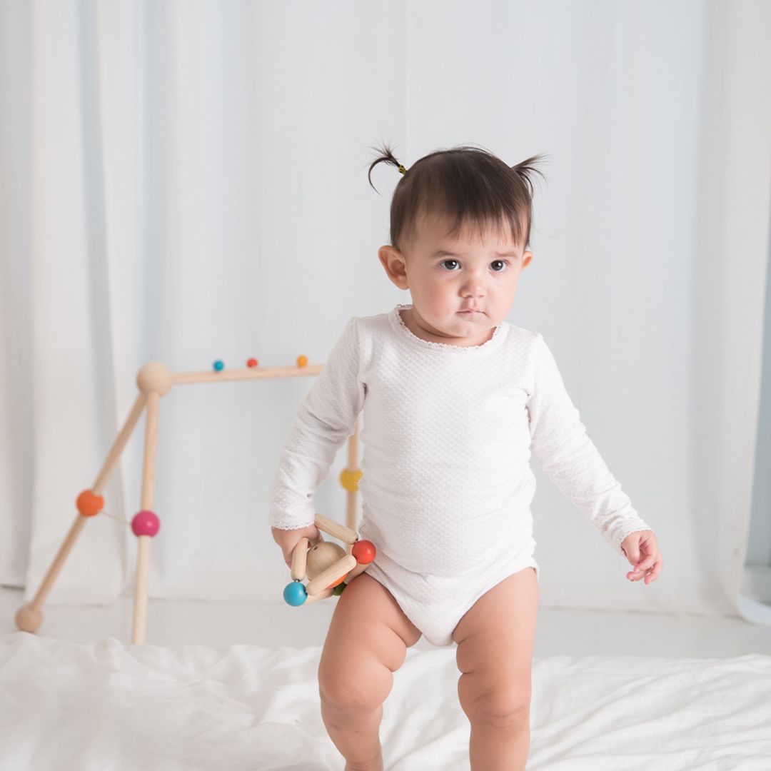 Child in a white onesie standing next to a colorful wooden toy on a white background