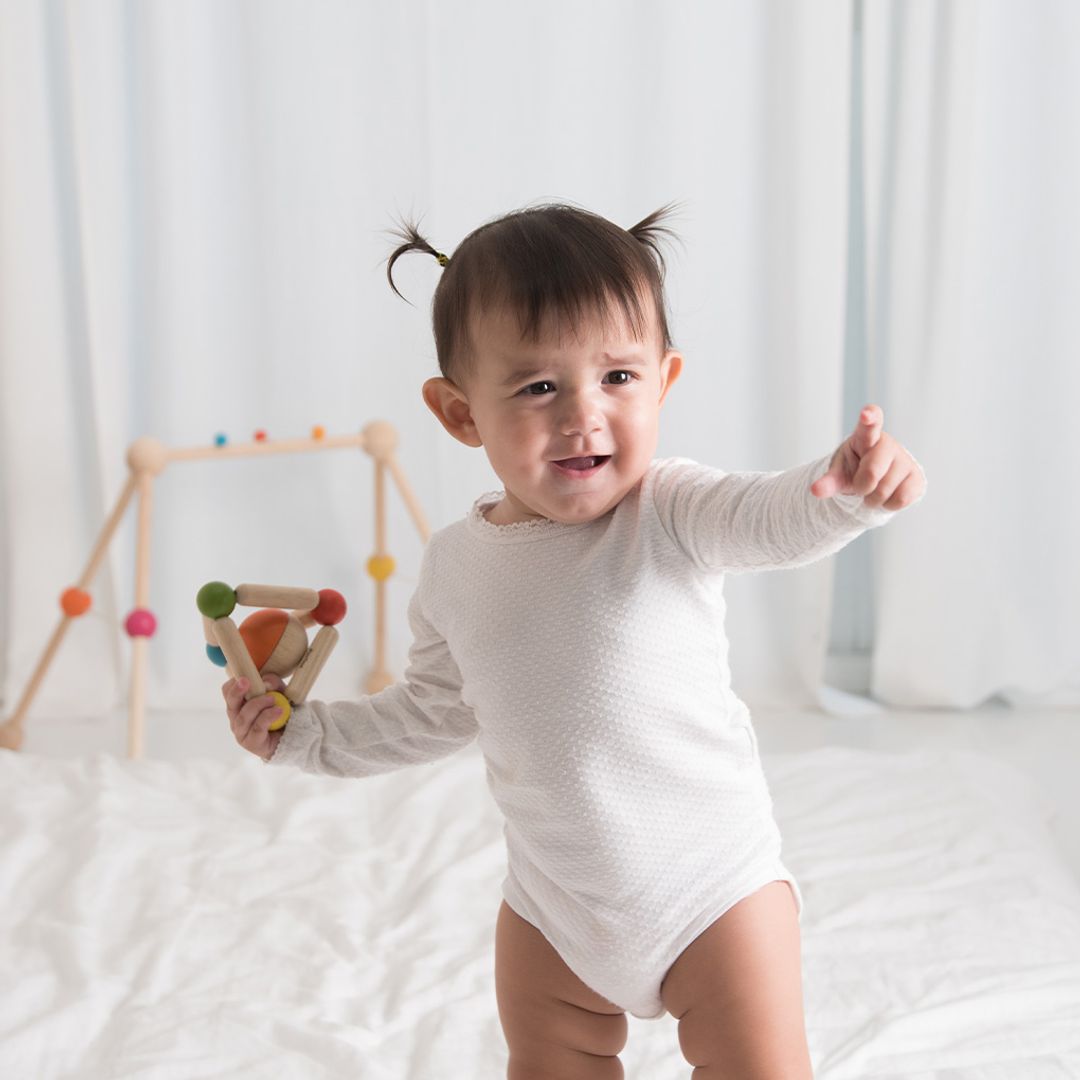 Baby in a white onesie holding a colorful toy against a white background