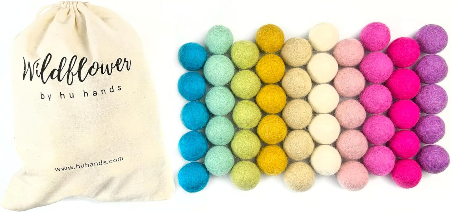 Colorful felt balls with a 'Wildflower by hu hands' drawstring bag on a white background