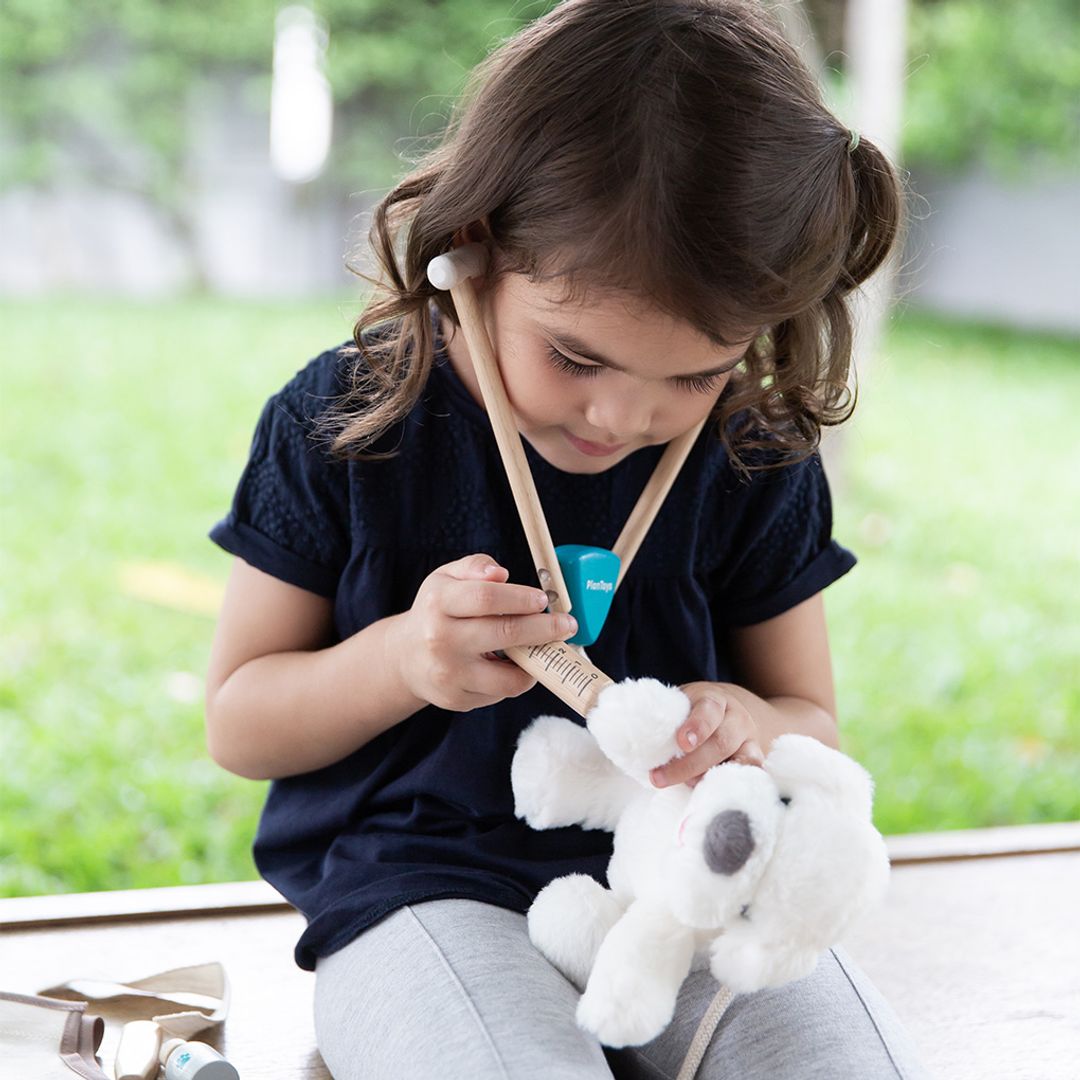 Child playing with drumsticks and a plush toy outdoors