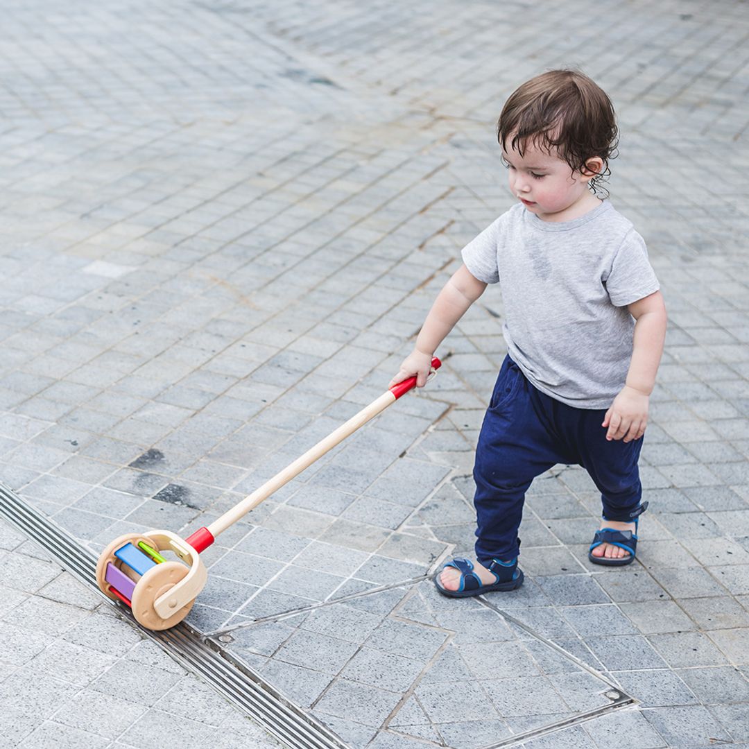Child pushing a colorful toy with wheels on a paved surface