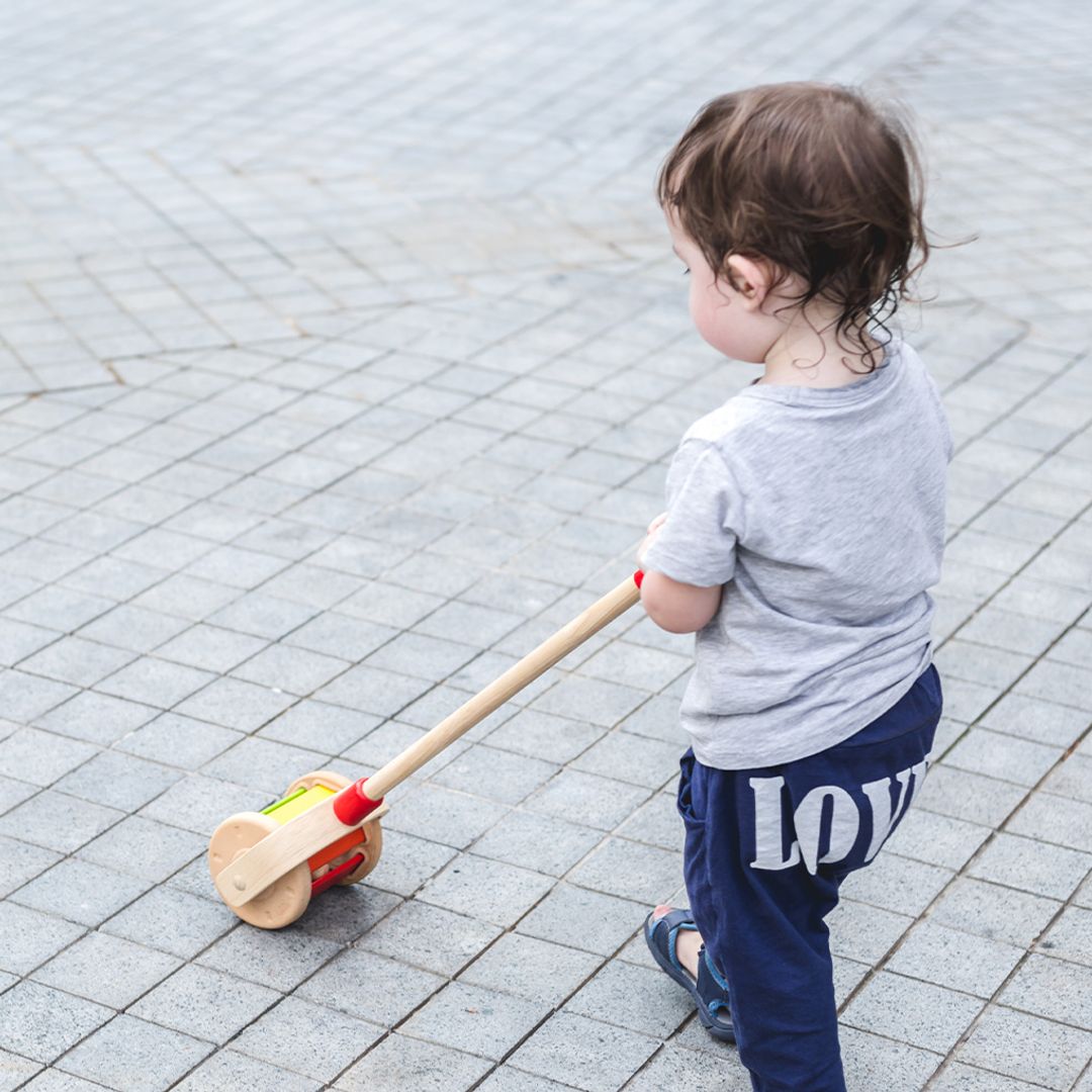 Child pushing a toy on a paved surface