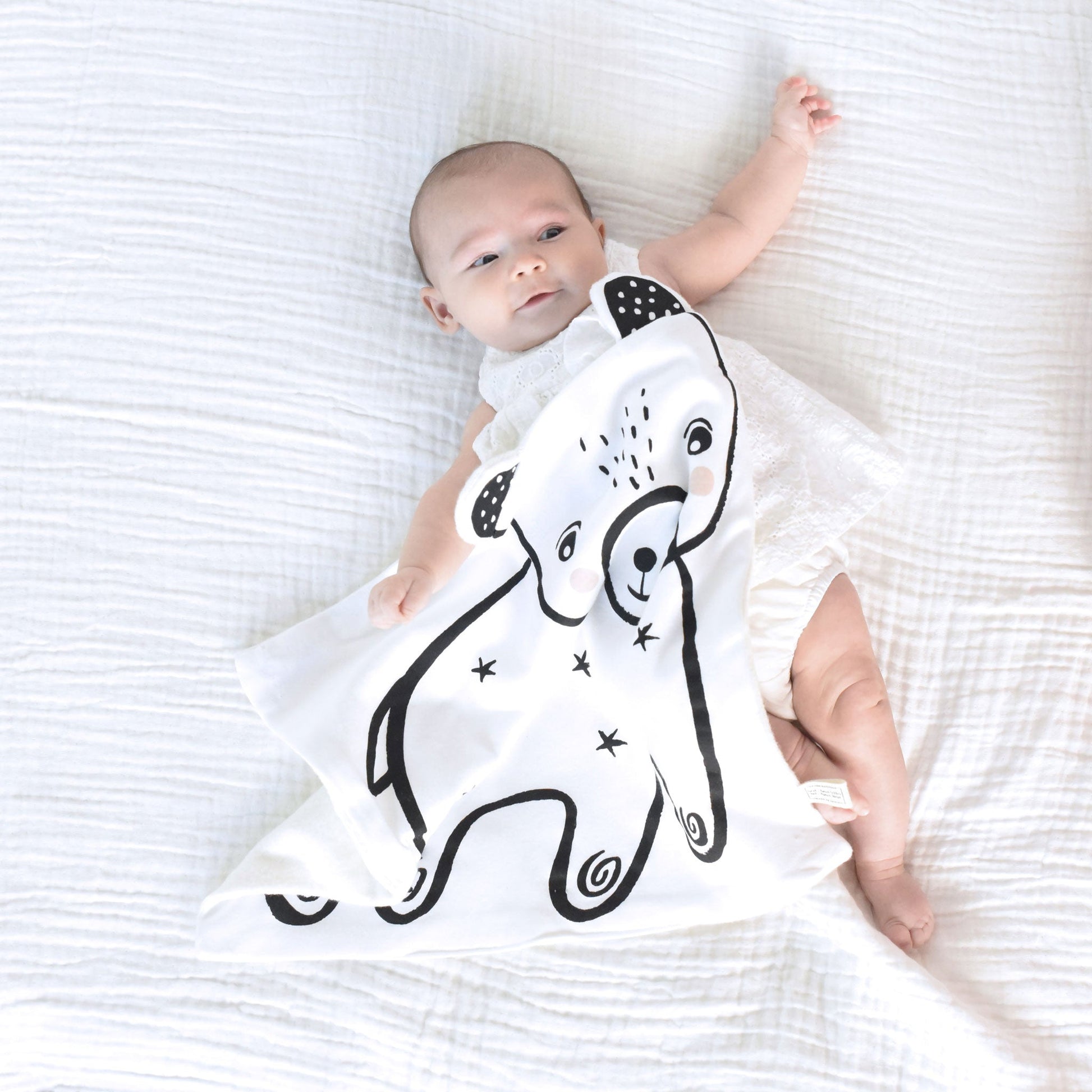 Baby lying on a white blanket wearing a onesie with a black and white design.