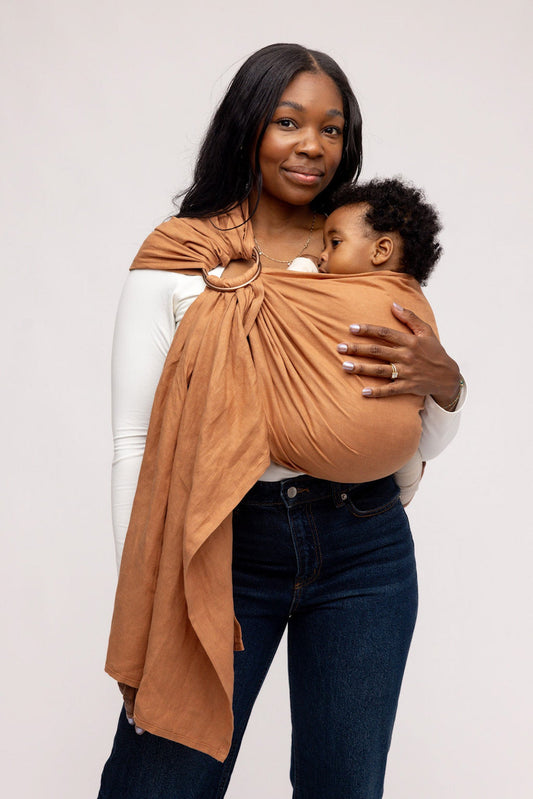 Woman holding a child in a brown baby carrier against a white background