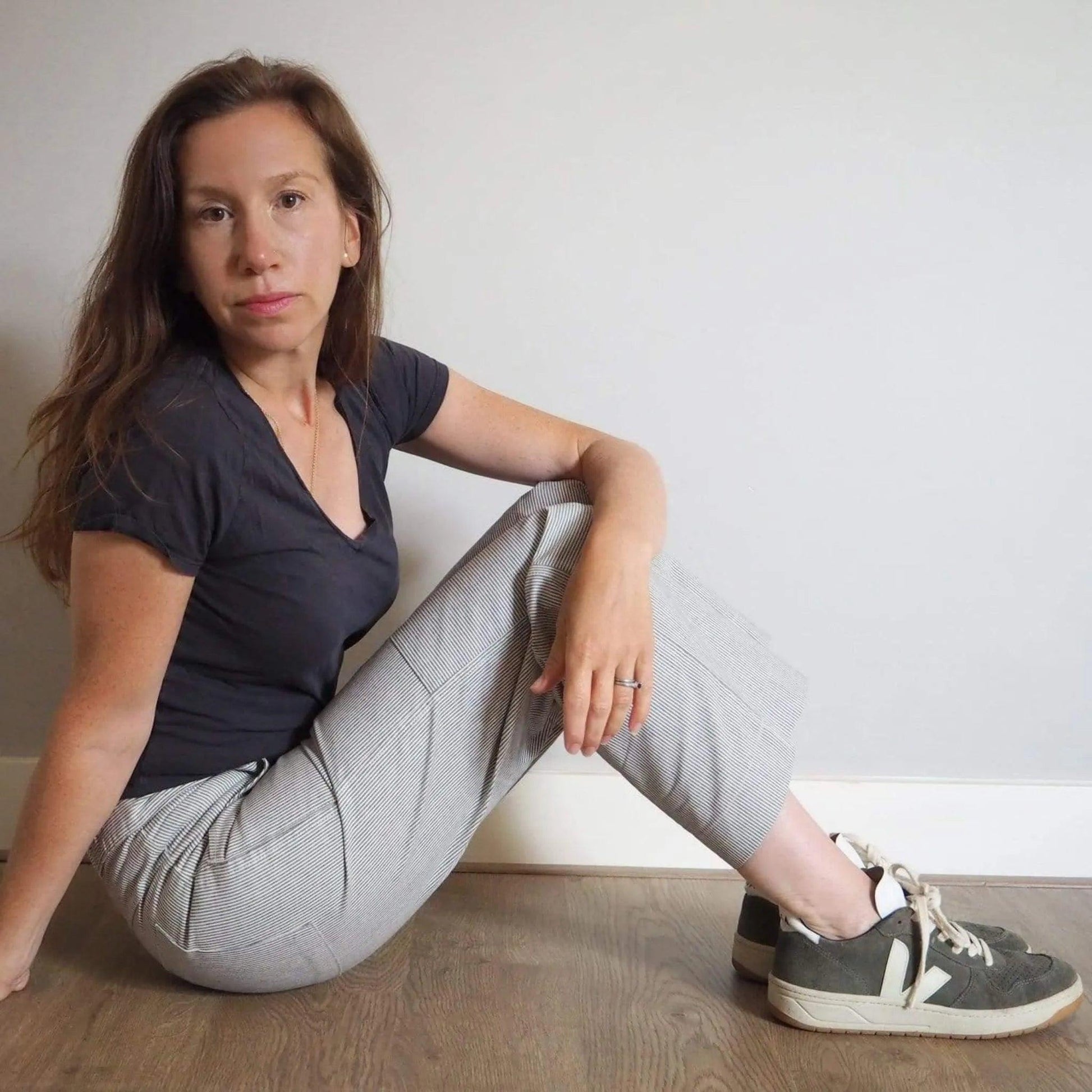 Woman sitting on the floor wearing a dark shirt and light gray pants.