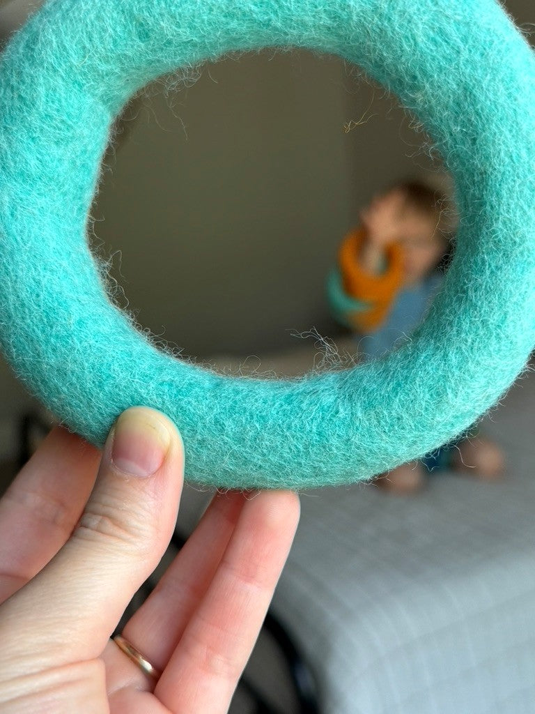 Turquoise felted yarn ball held by a hand with a blurred background