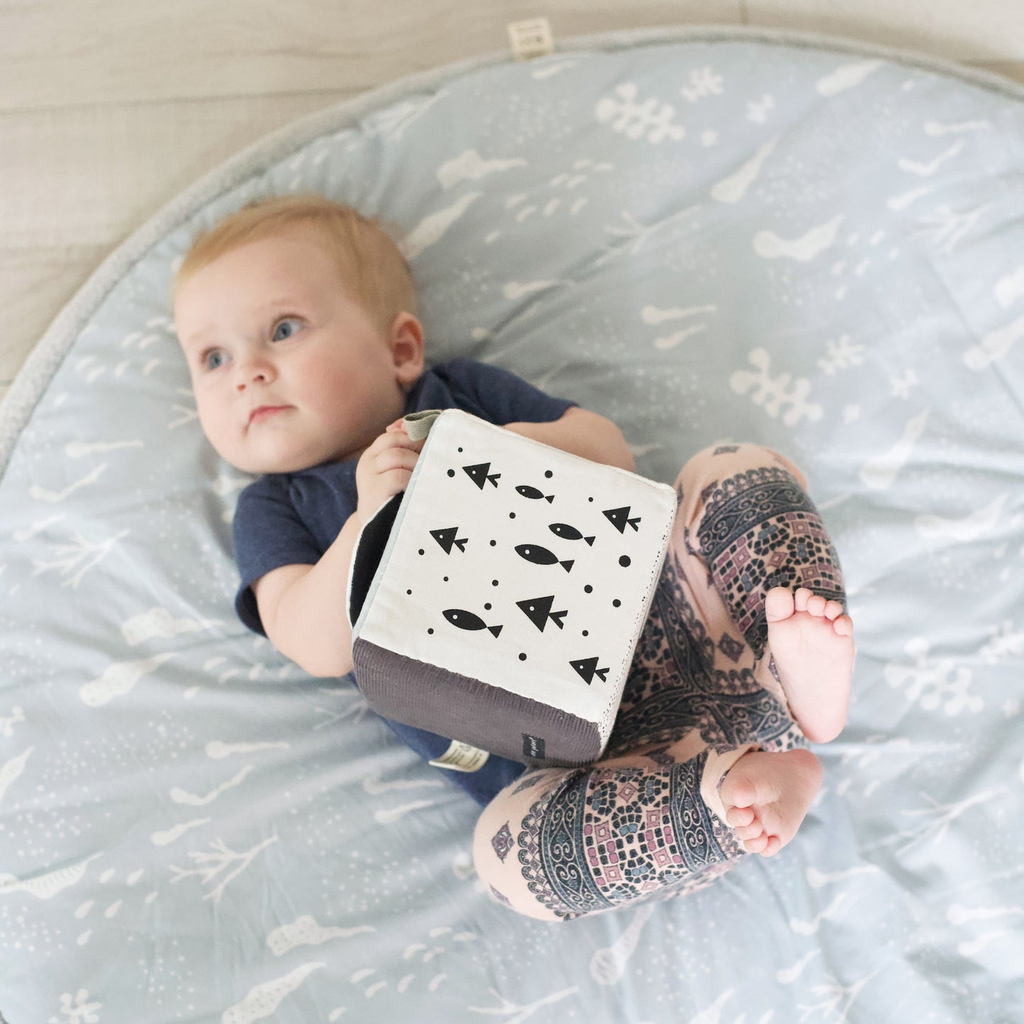 Baby lying on a patterned mat with a toy, wearing colorful socks.