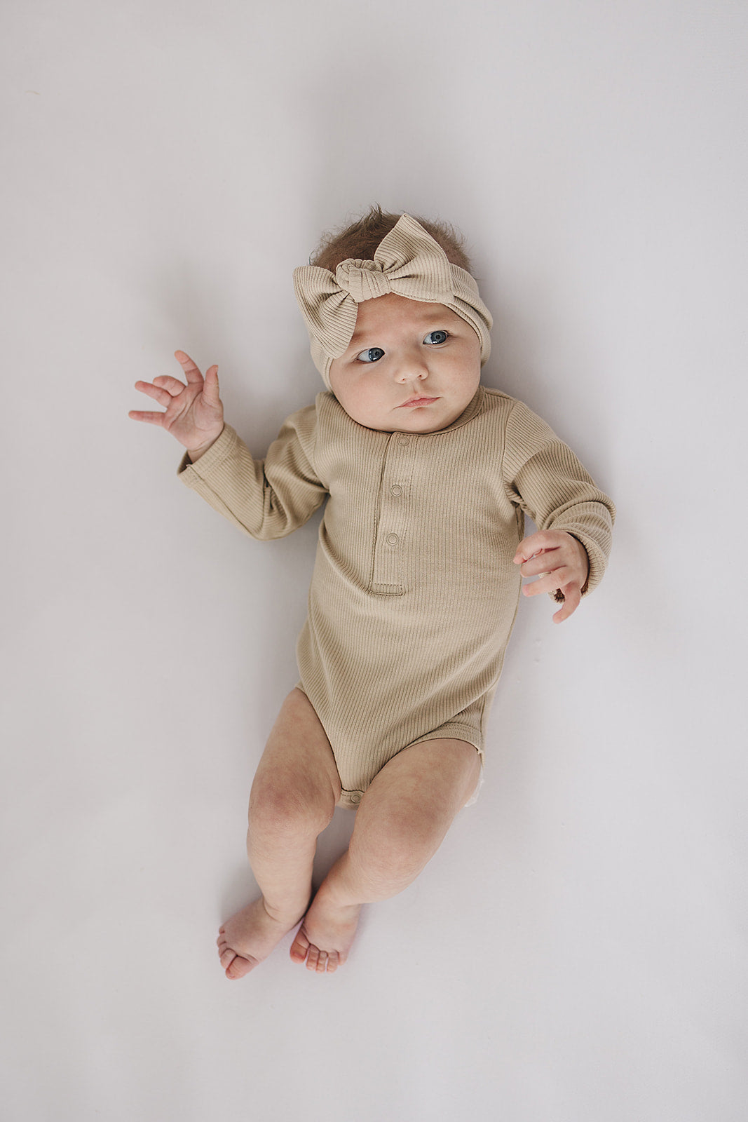 Baby wearing a beige onesie and headband on a light gray background