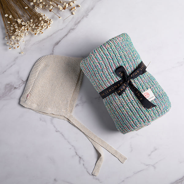 Knitted headband and blanket set on a marble surface with dried flowers.