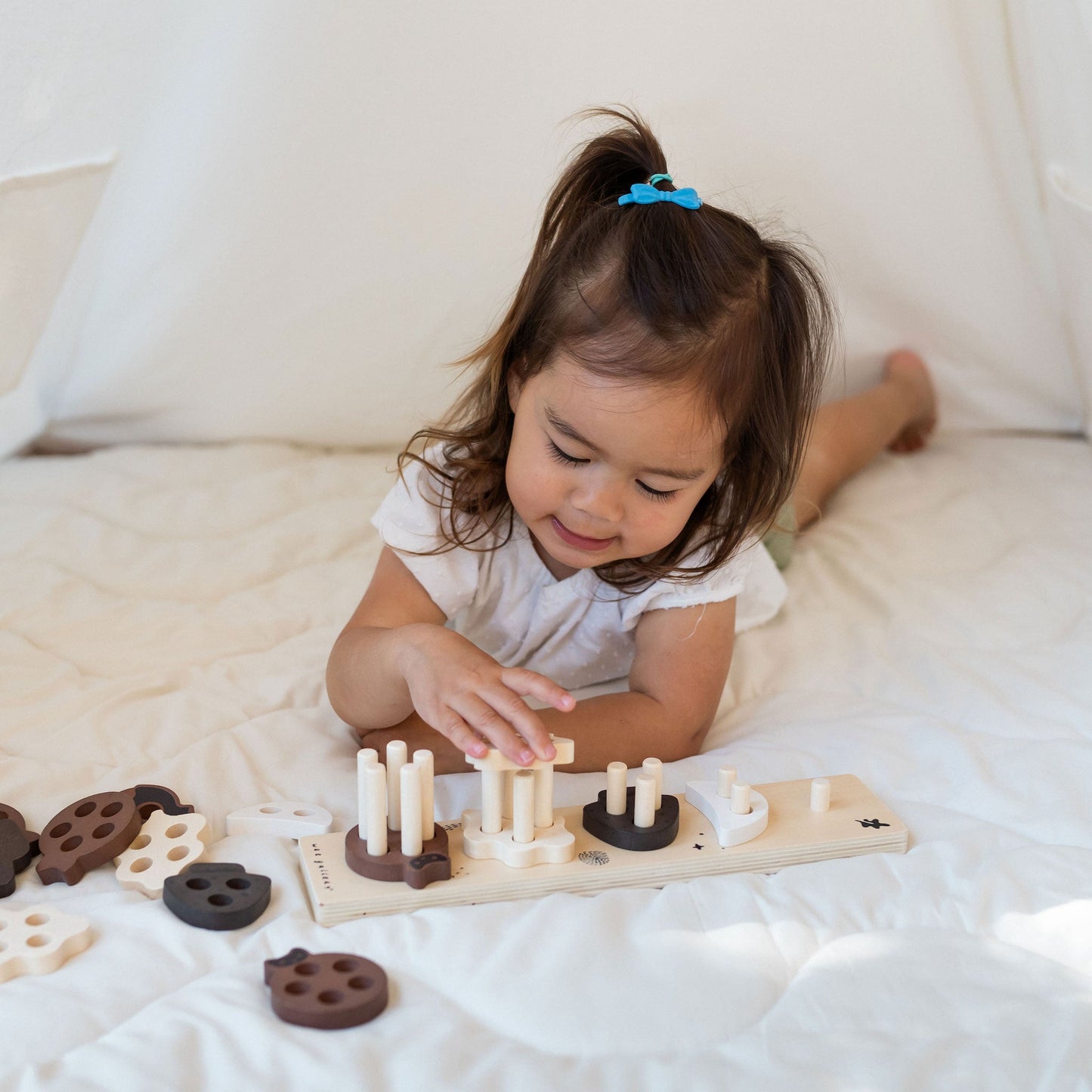 Child playing with a wooden puzzle on a white bed