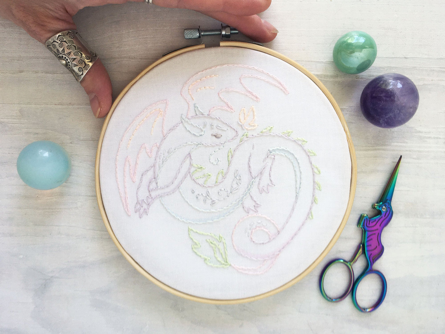 Embroidery hoop with dragon design, scissors, and colored stones on a light surface