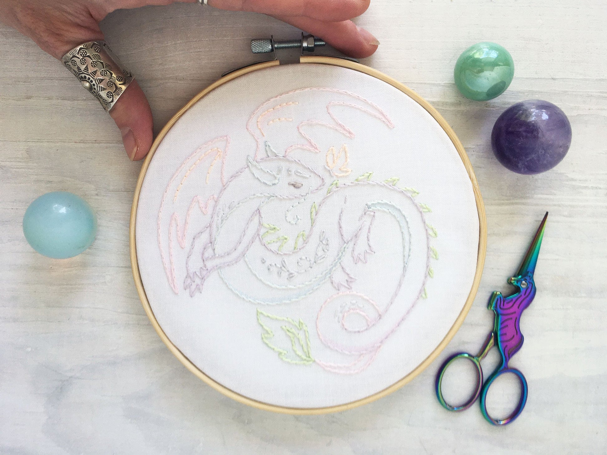 Embroidery hoop with dragon design, scissors, and colored stones on a light surface