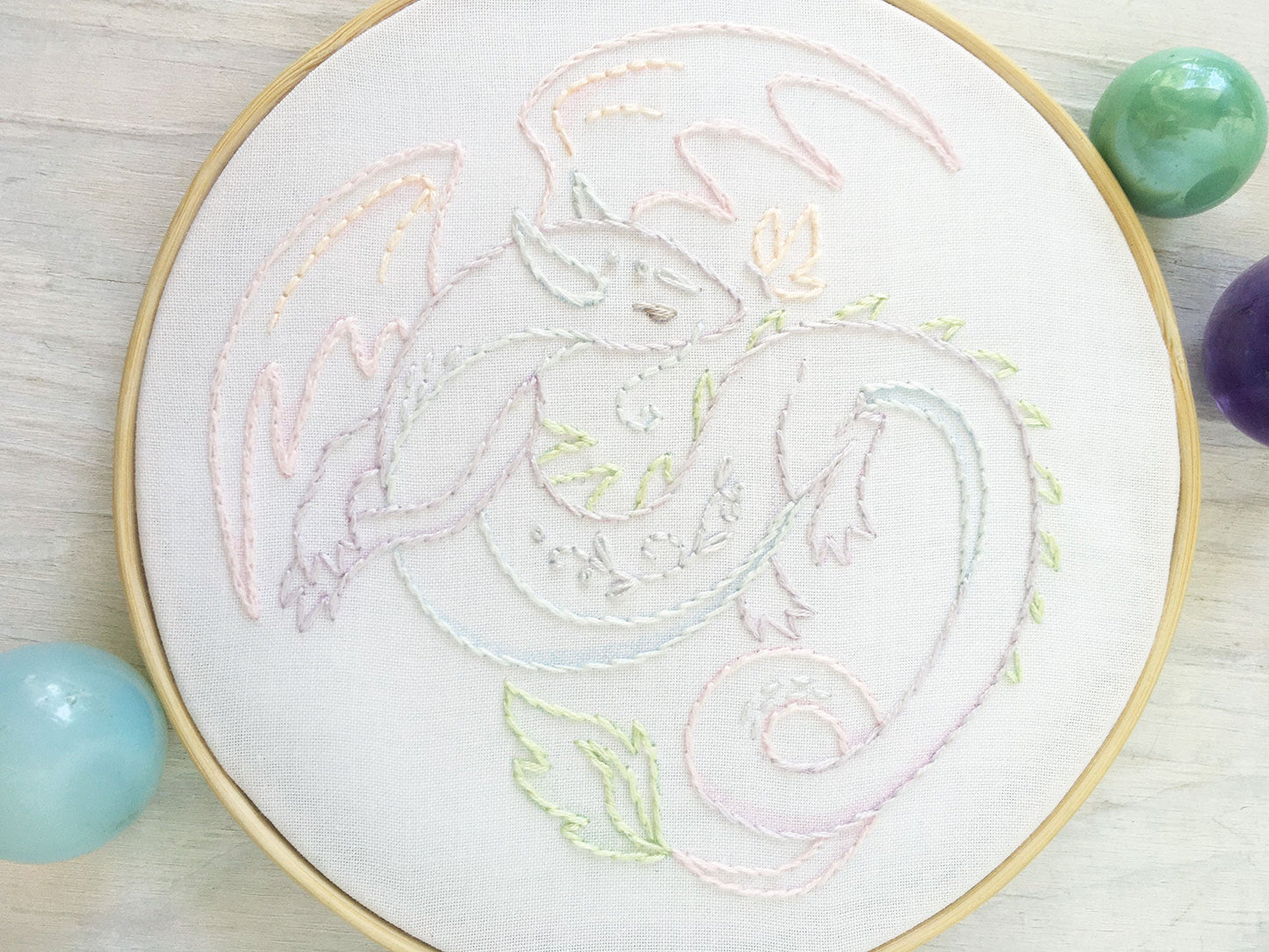 Embroidery hoop with a dragon design on white fabric, surrounded by colorful embroidery threads.