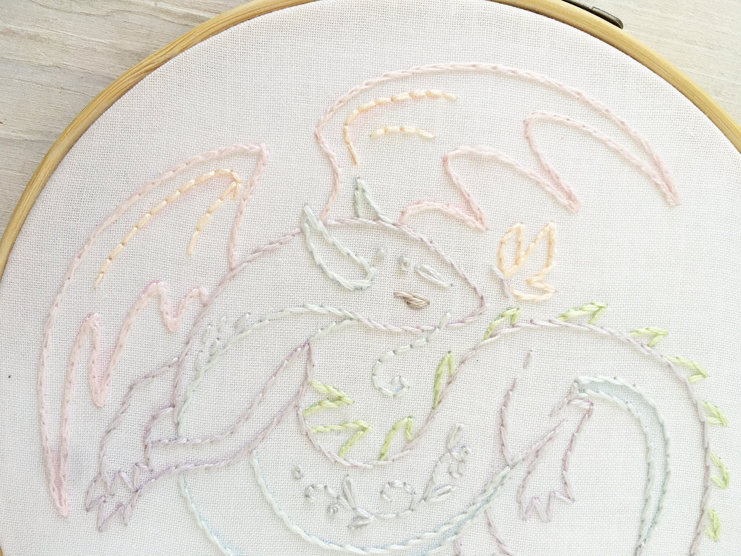 Embroidery of a dragon design on white fabric with a wooden hoop.