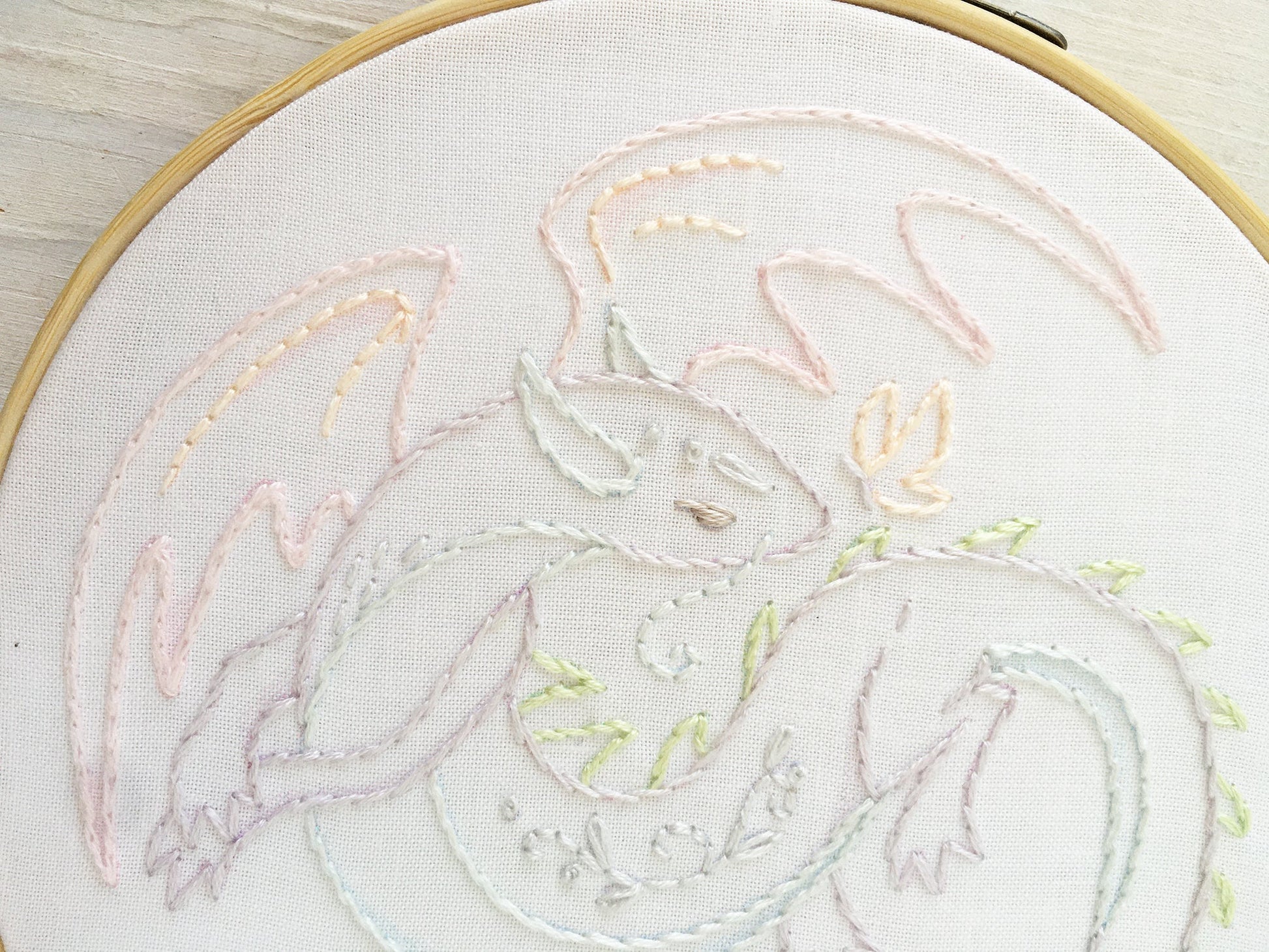 Embroidery of a dragon design on white fabric with a wooden hoop.