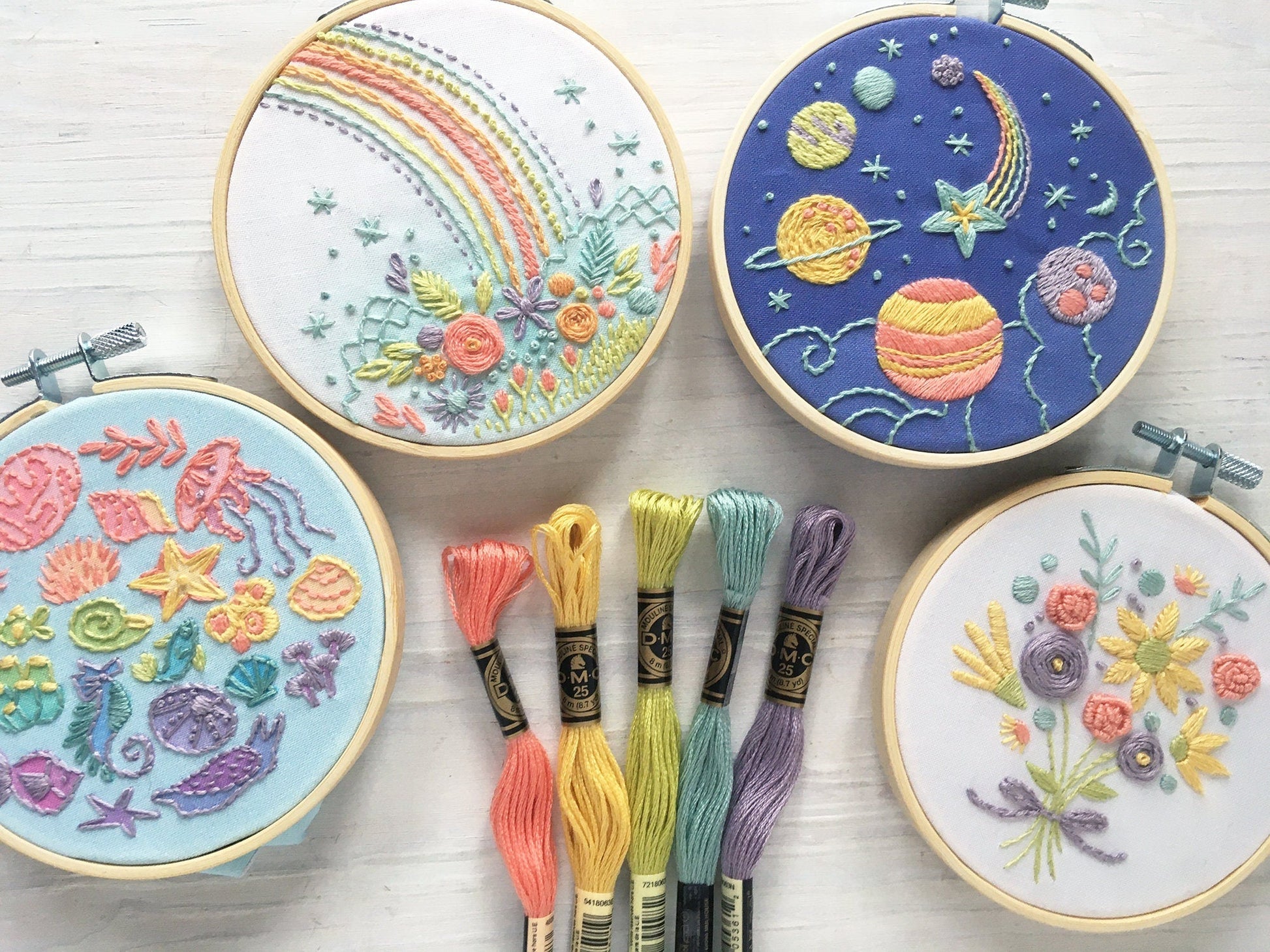 Four embroidery hoops with colorful stitched designs on a wooden surface.