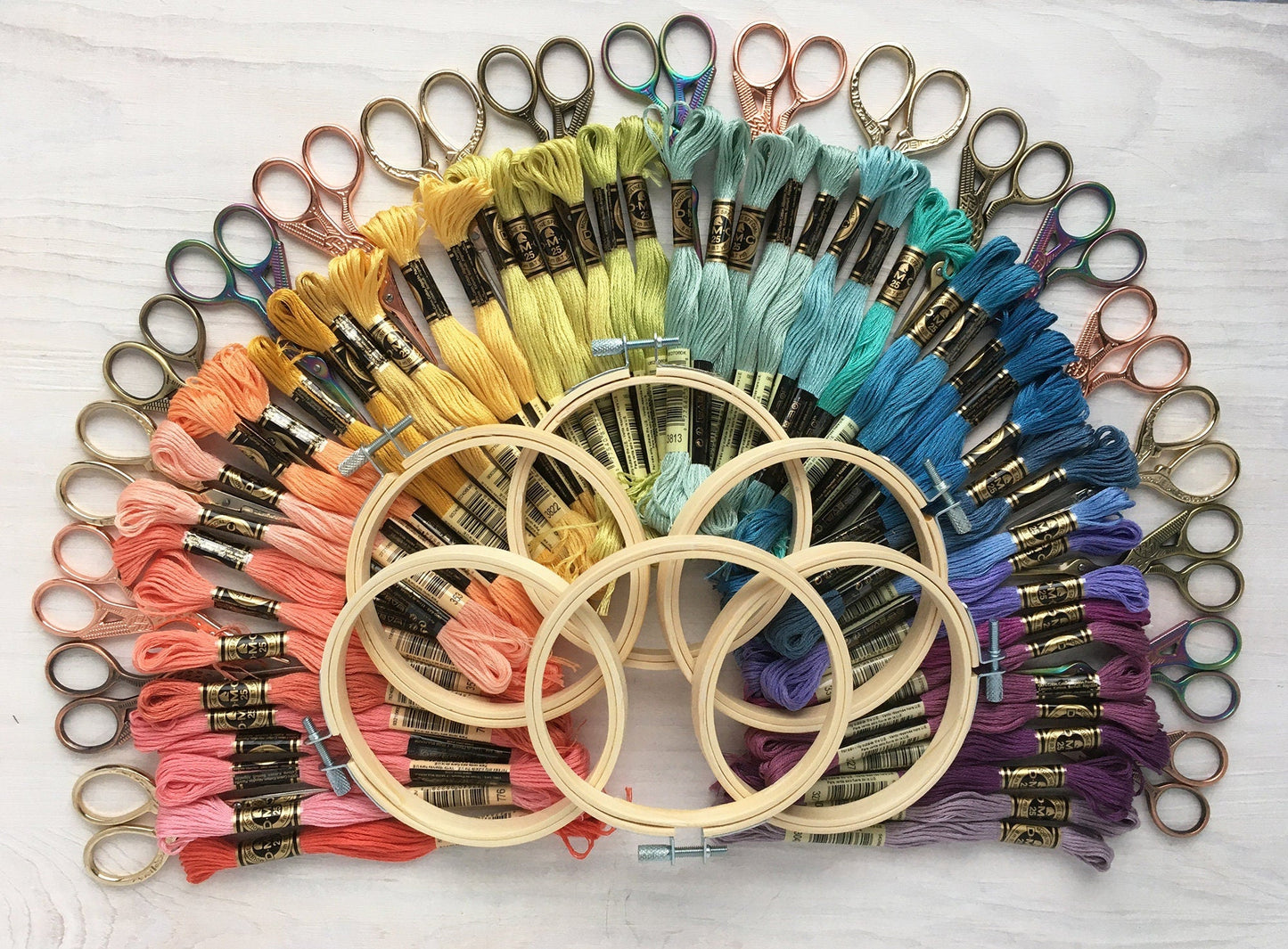 Embroidery hoops and colorful threads arranged in a circular pattern on a white surface.