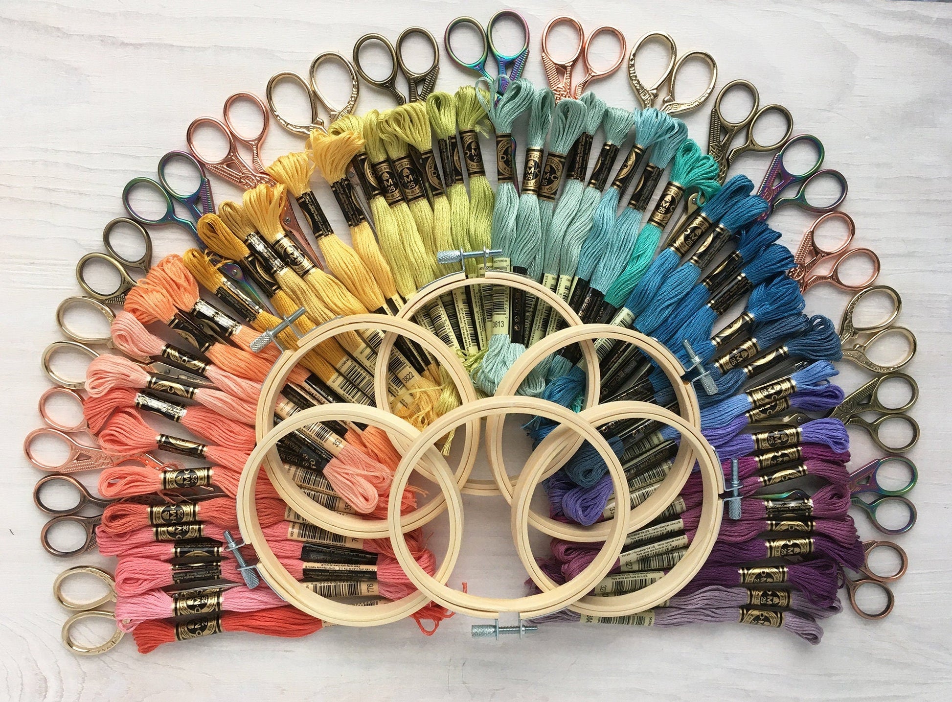 Embroidery hoops and colorful threads arranged in a circular pattern on a white surface.