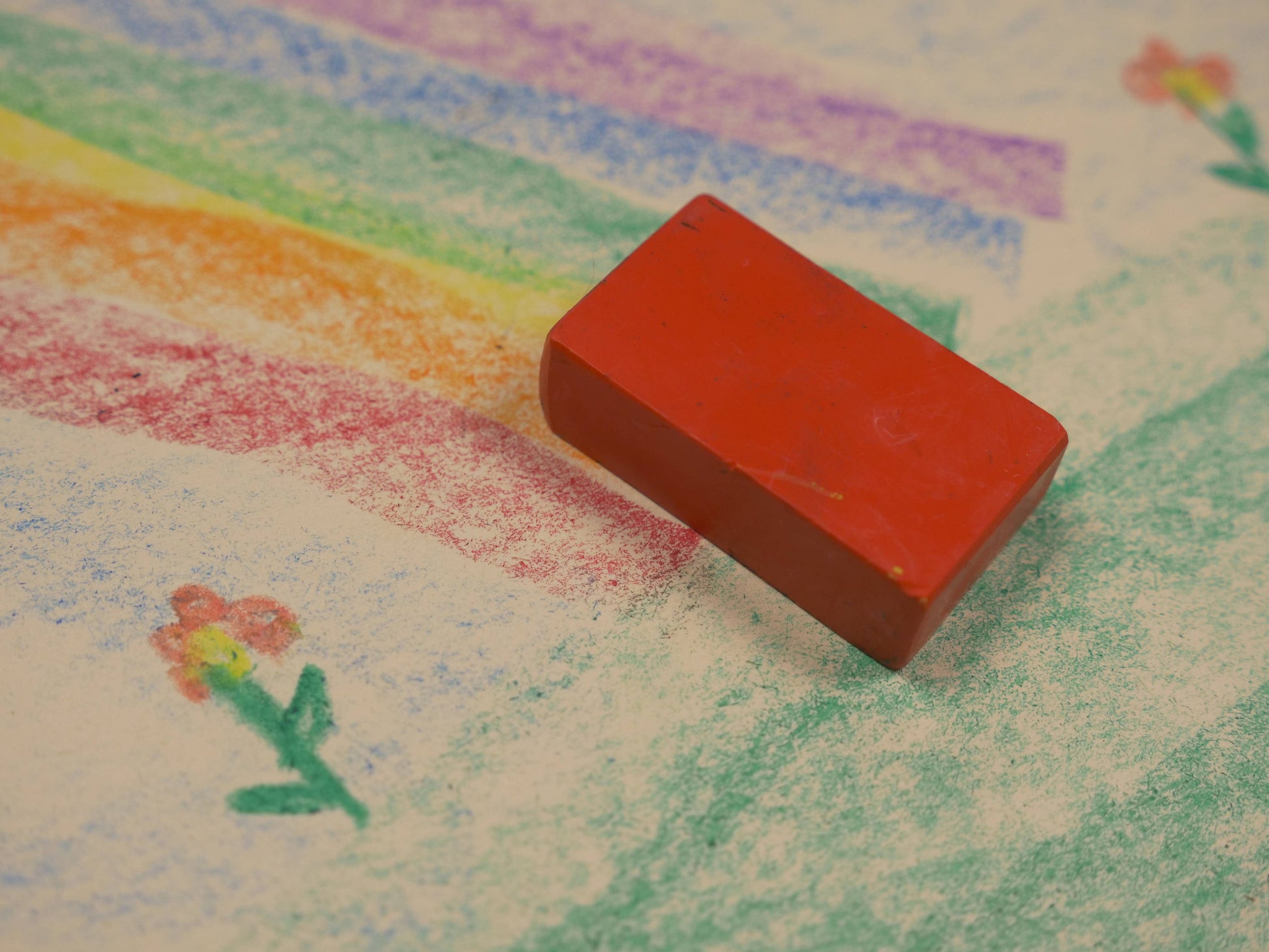 Red block crayon on a piece of paper with a colorful crayon drawing