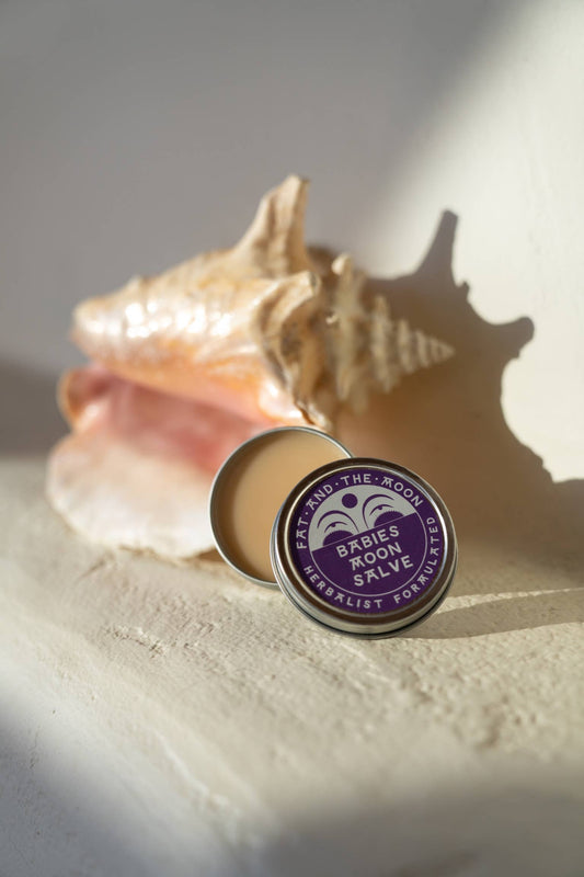 a tin of babies moon salve next to a sea shell