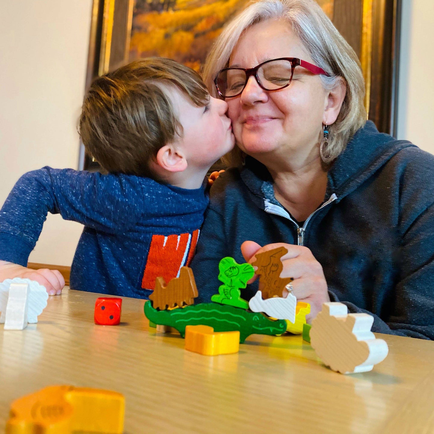 Child kissing an adult on the cheek while playing with wooden toys at a table.
