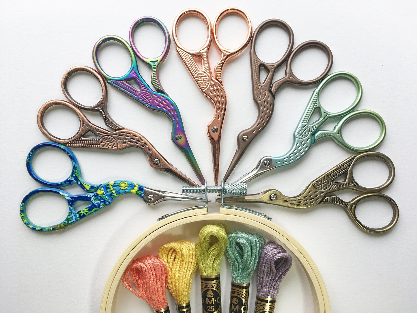 Set of colorful scissors arranged around a hoop with embroidery floss on a white background
