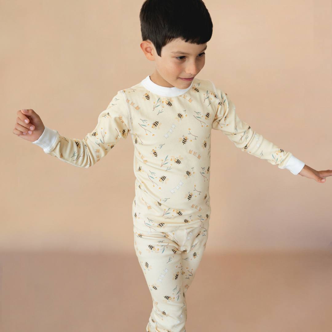 Child wearing a long-sleeve shirt and pants with a bee pattern on a beige background