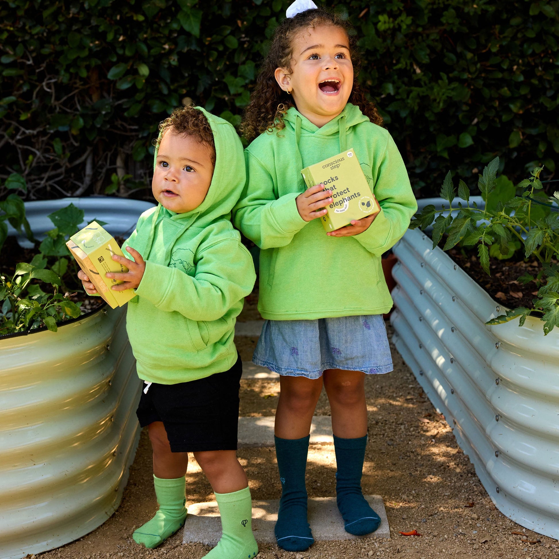 Two children in green hoodies holding books outdoors.