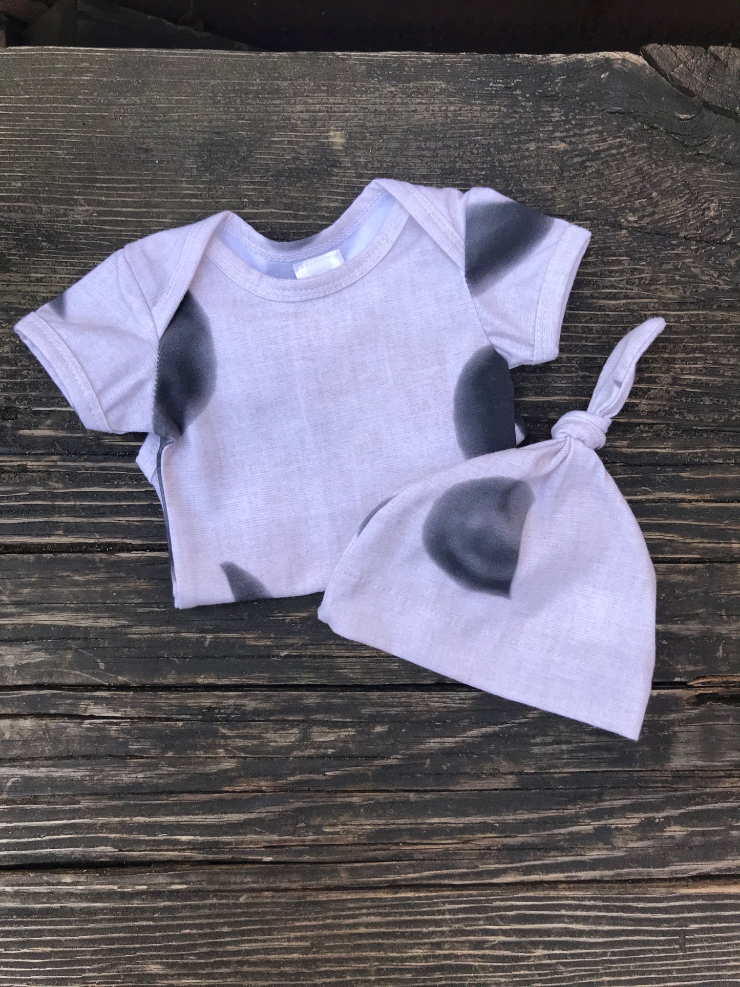 Short sleeve moon phase onesie with knot hat  on a wood bench