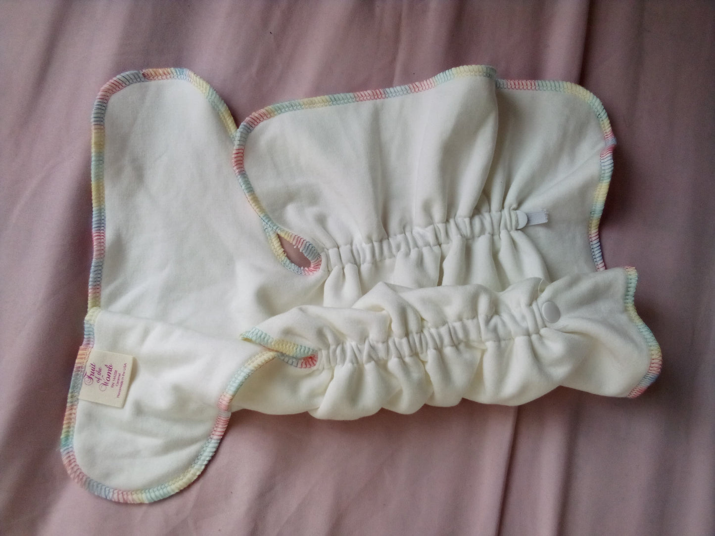 White baby blanket with colorful trim on a pink background