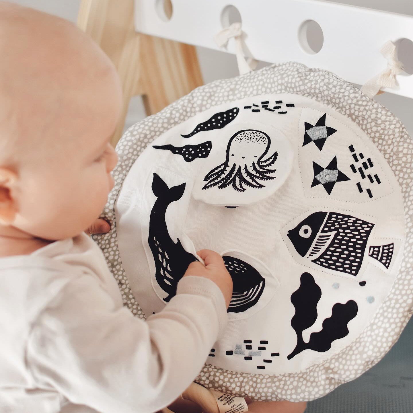 Baby interacting with a round, textured mat featuring black sea creature illustrations.