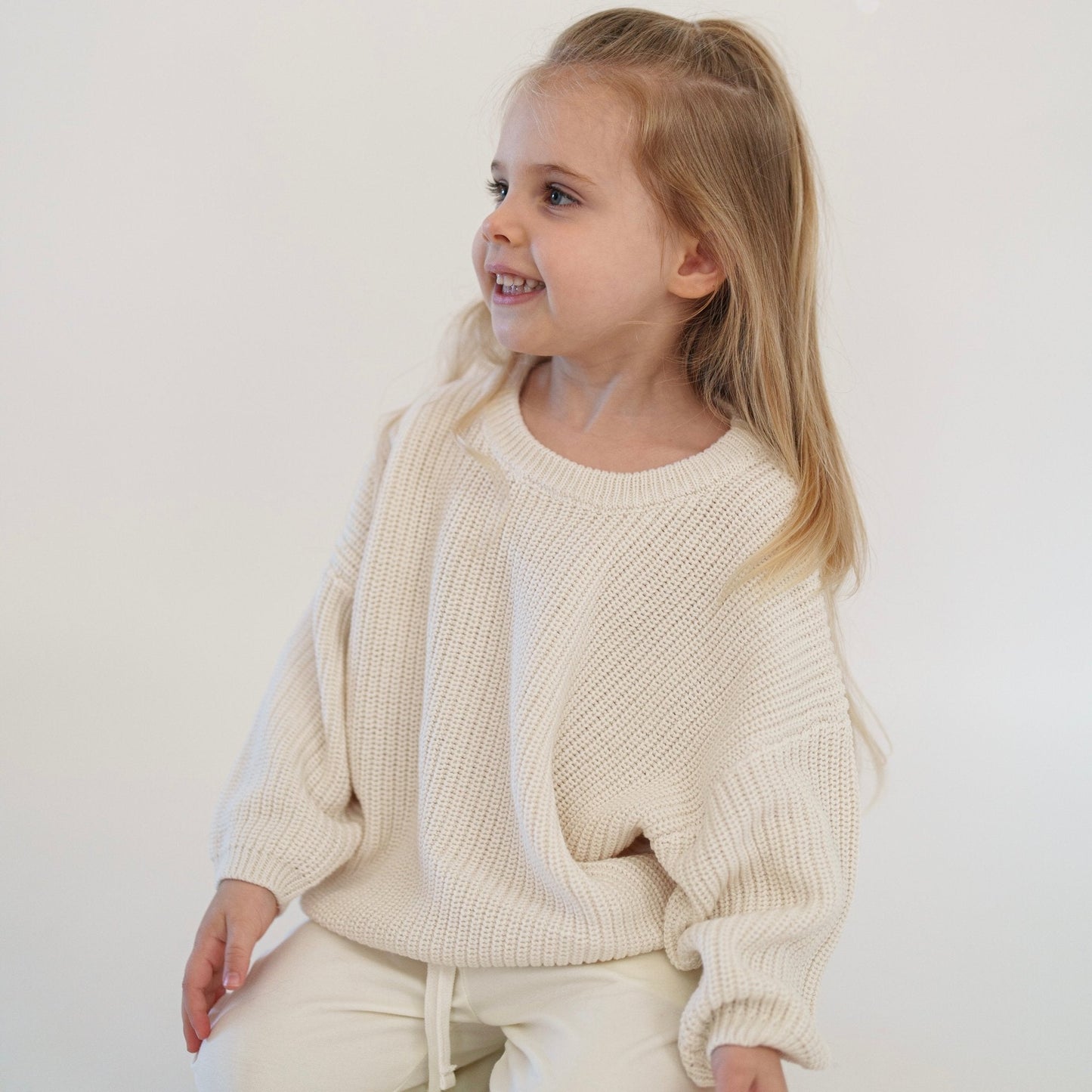 Young girl wearing a cream-colored knit outfit against a white background