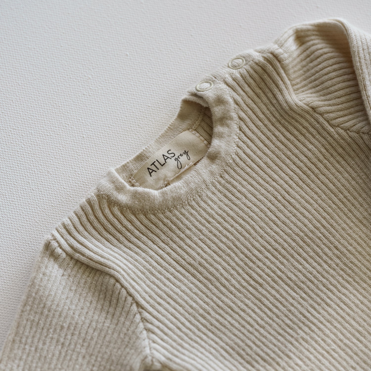 Beige ribbed sweater with 'Atlas' label on a light background