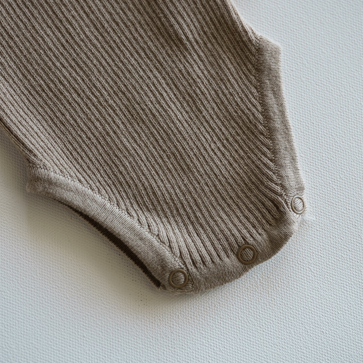 Brown ribbed baby onesie on a light gray background